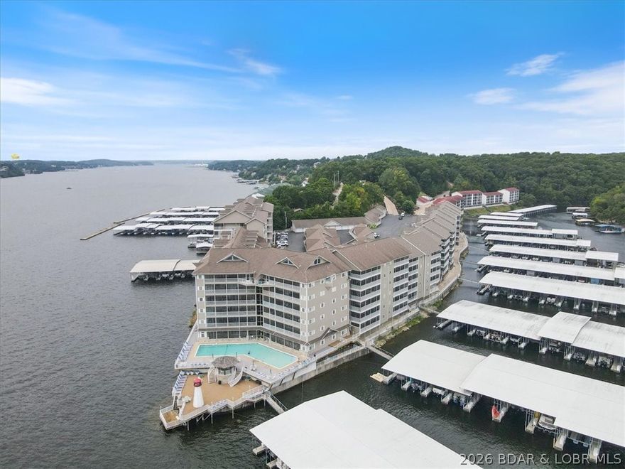 Enjoy exceptional lake living in this beautifully renovated condo offering stunning views of the main channel at Lake of the Ozarks. Convenient elevator access leads you directly to this unit with direct access to the pool and hot tub from the screened-in porch.
The updated open floor plan features a spacious dining area with a designer ceiling and a chef-inspired kitchen complete with stainless steel appliances, under-cabinet lighting, pantry, and bar seating. The large living room showcases an eye-catching fireplace and a wall of windows that capture incredible views of the pool and lake.
The primary suite offers peaceful lake views, private access to the enclosed porch, and a luxurious bath with a soaking tub, walk-in shower, double vanity, and walk-in closet. Two additional bedrooms, two more full baths, and a well-appointed laundry room with sink and an extra refrigerator provide ample room for guests and everyday convenience.
This condo is being offered turn-key furnished, including furniture, appliances, grills, and more—making it ready for immediate enjoyment. A 14x40 boat slip is located just a short distance from the condo door.