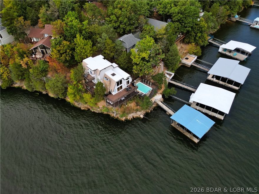 Make your Lake memories happen in this beautifully situated 5-bedroom, 4.5-bath home located in Tan-Tar-A Estates at the 26-mile marker—and best of all, there is NO Land Lease! This turn-key, nicely decorated property comes fully inclusive and ready for immediate enjoyment.  The exterior is designed for entertaining, featuring a 6' deep rectangular concrete swimming pool, Trek decks off every floor, and parking for up to five vehicles. You’ll enjoy stunning sunsets and perfect lake views from the expansive outdoor spaces.  Inside, the entry level offers a large bedroom with a full bath plus an additional half bath. A few steps up lead to two guest bedrooms and a shared bath. The main living area features a beautiful kitchen, dining space, and a living room with floor-to-ceiling windows and a cozy fireplace. The lower level provides a spacious relaxing area for TV and games, leading directly to the wrap-around deck and pool.  With a proven VRBO rental history available for qualified buyers and a motivated seller who has just dropped the price, this is a rare opportunity. Bring all reasonable offers today!