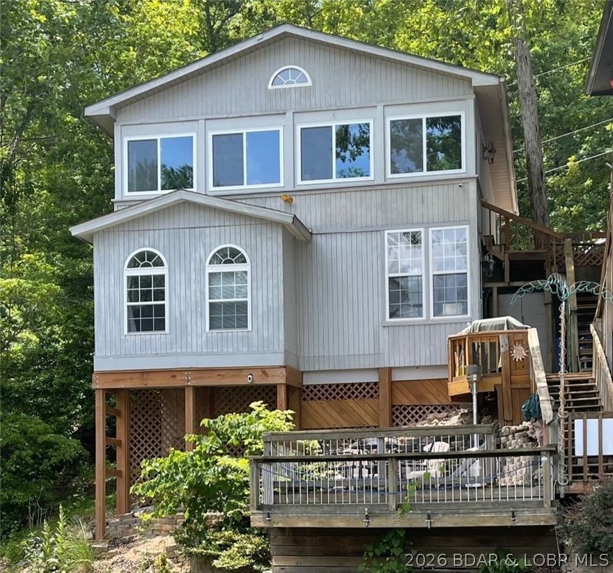 Discover peaceful lakefront living in this charming home tucked away in a quiet cove at the 6MM of the Gravois Arm. With 3 spacious bedrooms—including 2 with stunning lake views—this property is the perfect retreat for family fun or a relaxing escape. Enjoy a large eat-in kitchen, a three-season sunroom with windows and screens ideal for morning coffee or evening sunsets, and a lake-level deck where you can fish, unwind, or watch the kids play in the calm cove waters below. Recent updates include new vinyl plank flooring on the lower level, new A/C system for year-round comfort, extended deck-grilling niche, replaced outdoor wooden stairs, enclosed the covered deck to create a 3 seasons room, lighting, electrical & plumbing. The home sits on a quiet, dead-end road with no through traffic, has a martini deck, an exclusive boat slip & lift that accommodates up a 24’ boat. Lovingly maintained and currently a successful short-term rental, this home combines modern convenience with lakeside charm. Located in the always-popular Indian Creek area close to restaurants, marinas, and all the lake fun—while still enjoying your own relaxing get-away. Don't wait on this one!