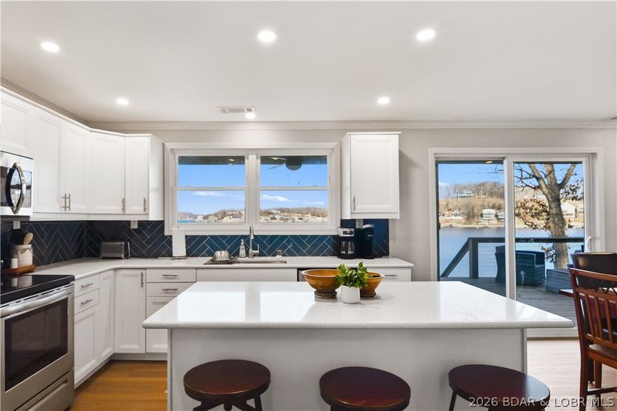 Charming, updated lakefront home at the 5 MM of Lake of the Ozarks offering deep year-round water, a wide cove view, and a gentle lot with plenty of parking. Tucked inside a wonderful cove, you get protection for swimming and boating while still enjoying a big, beautiful water backdrop. This 3BR, 2BA home shows exceptionally well with modern colors and extensive updates including new drywall, newer windows, fresh paint, doors, flooring, fixtures, faucets, vanities, and a completely remodeled kitchen featuring quartz countertops and stainless appliances. The view from the kitchen sink straight out to the lake is exactly what lake living should be. Two large living areas provide flexibility for entertaining or hosting guests. Outdoor space is dialed in with a fenced yard and recently rebuilt lakeside decks perfect for relaxing or gathering. The dock features two slips (12x31 and 12x28) and sits in deep water year-round. Being sold very nicely furnished and turnkey, this home truly comes ready for immediate enjoyment. A well-updated home, strong dock, gentle lot, and ideal cove location make this a complete lake package.  Blacktop roads to the home and plenty of storage!