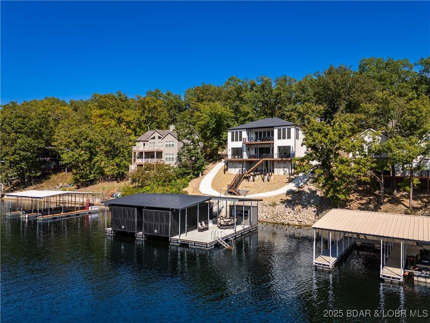Modern Lakefront Perfection at Lake of the Ozarks! This exceptional newer-construction home offers 3,615 sq ft of luxury and style. Featuring 4 bedrooms (3 having direct access to your waterfront decks), 3.5 baths, and being sold turn-key with high-end finishes and designer furnishings, this property is ready for you to start enjoying lake life immediately. Built for entertaining, the open floor plan features a spacious kitchen with premium appliances, custom cabinetry, and a large island that flows seamlessly into the dining and living areas. Floor-to-ceiling windows bring in natural light and frame the beautiful lake views. Step outside to enjoy a true entertainer’s paradise. A wrap-around cart path leads to a brand-new concrete dock, perfectly positioned in deep water with excellent protection and easy access to the main channel. The dock was made for fun and convenience - complete with a tiki bar, touchless boat covers, and ample space to host family and friends. Whether you’re lounging by the water, enjoying a drink at the bar, or heading out for a sunset cruise, this home combines modern comfort, style, and convenience in one remarkable lakefront package!