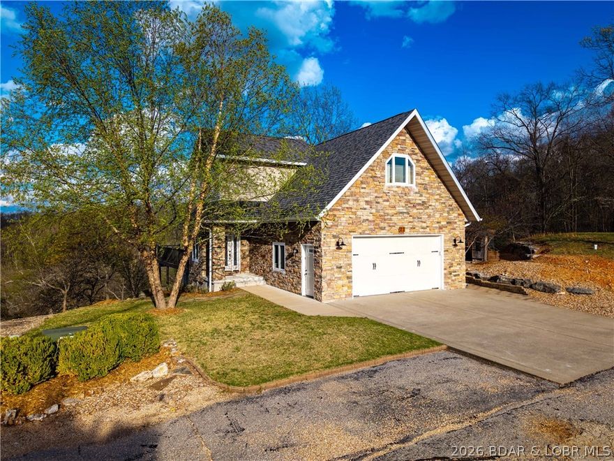 Discover the perfect blend of elegance and lakefront living in this stunning home overlooking the Big Niangua arm. From the moment you arrive, stone accents and manicured landscaping deliver undeniable curb appeal. Inside, the wall of windows in the living room invites the lake into your space! The kitchen shines with fingerprint-resistant stainless appliances, a huge pantry, and expansive counter space. The upper level features a secluded master suite—a true sanctuary with a spacious walk-in closet and a modern bathroom with sleek quartz vanities. Your guests will have their own private lower-level quarters, complete with two bedrooms and a full bath. For those needing extra elbow room, the enclosed finished deck serves as a versatile space for a home gym, hobby or tv room. Outdoor living is where this property truly excels. Host unforgettable dinners on the covered entertaining deck or hop in your golf cart for a quick trip down to the water. A private 12'x34' boat slip at the community dock includes a swim platform, making it easy to dive into the lake life. An extra-large two-car garage and a storage room for all your gear, this home is as practical as it is beautiful.