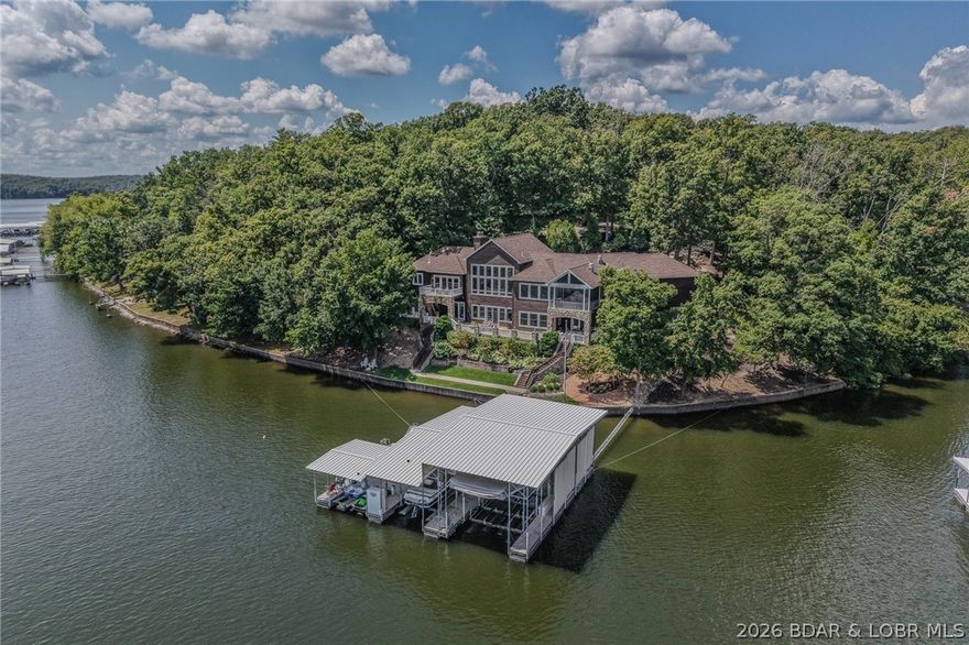 Positioned within an exclusive gated estate situated on 10.7 fully fenced acres in Osage Beach, this exceptional lakefront residence offers rare privacy and sweeping views of untouched state park shoreline. Encompassing 7,500 sq ft with 850’ of shoreline, it delivers a refined lake lifestyle with an impressive private dock. A grand entry showcases soaring vaulted beam ceilings and walls of glass capturing breathtaking water views. The chef’s kitchen flows seamlessly into expansive living areas and a screened porch with commercial-grade exhaust for year-round entertaining. Featuring 6 bedrooms, a private office/den, 6 full baths, and 2 half baths, the home is anchored by a luxurious primary suite with steam shower and oversized boutique-style closet with island. The walkout lower level offers a theater, bar, and game area, with additional bar service on the main level and dock. The dock includes a 16x48 slip with 30,000 lb lift, 12x30 slip with lift, and double PWC slip with lift. Additional amenities include attached and detached 3-car garages, climate-controlled gym, and RV pad with electric. Pre-listing inspected with a one-year home warranty included.