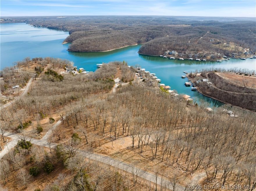 6.4 acres stretching from Pisces Dr and wrapping around to Ivory Cir at the 24MM of Lake of the Ozarks, offering elevated south-facing views toward Kinchlow Hollow Cove with the potential to further open the lakeview through selective tree clearing. The property presents multiple building site options depending on your vision, including elevated settings off Pisces with sweeping views and moderately sloped areas near the center that would accommodate walkout designs while maintaining privacy. Natural rock outcroppings add character and texture to the landscape, and paved road access with electric nearby makes development straightforward. CoMo fiber internet is available. Located just around the bend from Paradise Restaurant, approximately 4 miles to Shawnee Bend Boat Ramp, with potential boat slip rental at Riviera RV Resort, and convenient to Woods, Dollar General, and Sunrise True Value Hardware, this acreage combines view, usability, and location in one versatile tract.