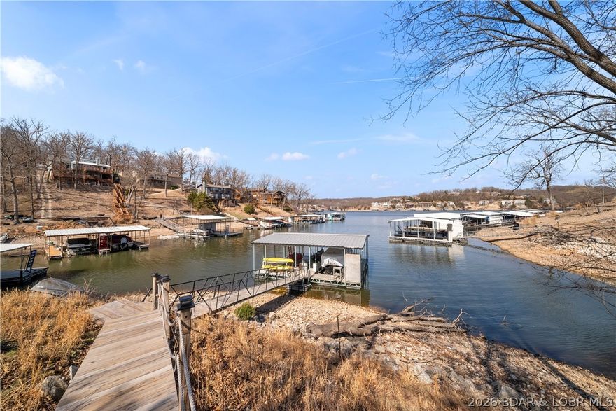 Offering approximately 4,000 sq ft, this 4-bedroom, 3-bath home features a spacious open great room with a cozy wood-burning fireplace and a wall of windows showcasing beautiful wooded and lake views. The walk-out lower level adds additional entertaining space with a large family room and kitchen/bar area ideal for hosting guests or relaxing after a day on the water. 
Nestled in the peaceful waters of Linn Creek Cove at the 31 Mile Marker, this lakefront home in Camdenton offers the perfect combination of privacy, space, and lake living. Situated on .78 acres and surrounded by mature trees, this property delivers a serene setting in one of Lake of the Ozarks’ most desirable quiet coves.
The loft-style primary suite offers a private retreat complete with its own bathroom and walk-in closet. Outside, enjoy true waterfront living with your private dock and boat slip, perfect for boating, fishing, and lakefront entertaining. Located in the sought-after Three Rivers Subdivision, this property combines peaceful cove protection with convenient access to the main channel and all Lake of the Ozarks has to offer. View virtual tour!