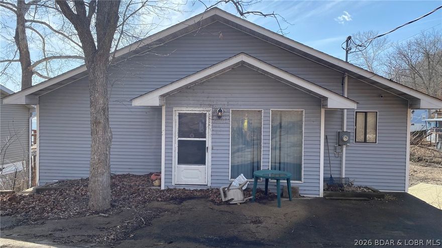 Attention flippers, remodelers, and investors! This lakefront “Diamond in the Rough” awaits your vision. Built in 1981 with over 1,700 sq. ft., the home offers 3 bedrooms, 3 baths, and a finished walkout lower level with family room, wood-burning fireplace, wet bar/rec area, utility/laundry space, and full kitchen—ideal for your ultimate Lakefront family retreat. The floor plan provides a solid foundation for updates and modern finishes. Upstairs, the primary suite and lake-facing second bedroom both feature sliding glass doors opening to beautiful views of the upper Gravois Arm of Lake of the Ozarks. Outside, the former two-level deck footprint is ready for your custom rebuild, creating the perfect space for outdoor entertaining. The property includes maintenance-free vinyl siding, 75 feet of shoreline, and a "never grounded" 2-well concrete dock with boat lifts included. Recent updates include a high-efficiency HVAC system, tankless water heater, and improved septic system. Community well water is just $200/year. This is a rare opportunity to own an original, unaltered lakefront home primed for your vision and value-added potential for a family retreat or income producing rental.