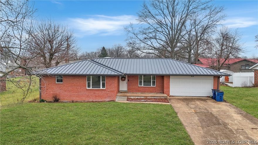 1960s brick beauty in Eldon city limits—neighborhood heart, fully reborn.Can you say NEW, NEW NEW! This is a MUST SEE! Outside you'll find New metal roof, gutters, fascia, landscaping, covered front porch, backyard patio. Inside Three beds, with one en-suite, two baths (walk-in shower), stainless LG kitchen appliances, gleaming granite countertops, crisp cabinetry, gas range, recessed can lighting, new fan/lighting that whispers cool air and glows just right. Cozy white-stone fireplace with electric insert. Newer windows throughout, bright, energy-smart, no drafts. 1800 sqft of pristine living, new luxury vinyl plank flooring —plus 1800 sqft of blank-canvas basement: half-bath rough-in, laundry, workshop. Feel the charm. Stunning & priced sharp!