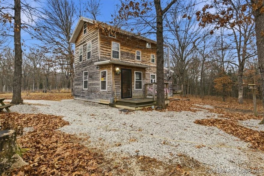 Tucked away on approximately 10 wooded acres just outside Cole Camp, this cedar-sided cabin offers privacy, functionality, and a well-thought-out setup for rural living. This three story home features roughly 1,200 square feet with three bedrooms and one bathroom, creating a unique and efficient use of space. Warm wood finishes throughout enhance the cabin feel. Heating is designed for efficiency and flexibility with a wood burning stove, electric mini splits and diesel heater. The upper level provides additional living or sleeping space. Infrastructure is already in place for a more self-sustained lifestyle. The 25x55 shop with a concrete floor offers excellent workspace and storage, complete with separate back room and loft that could be finished for additional use. Multiple outbuildings, a greenhouse, fenced garden area with raised beds, chicken coop, and a storm shelter add to the property’s functionality. The setting is quiet and private, yet still accessible, and located within the Cole Camp School District. This is a well-maintained property suited for those seeking a secluded retreat, hobby farm, or off-grid-inspired lifestyle with improvements already in place.