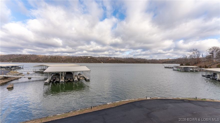 Opportunities like a this 6 bedroom condo are RARE!! 6 bedrooms & 3 bathrooms on the water, no unit above you, with two full levels, is an incredible value for the space. Freshly painted with updated countertops and fixtures, this unit offers a bright, open main level and panoramic lake views from the living room, kitchen and 4 bedrooms for a true “on-the-water” feel. The primary suite features a private bath, stone wood-burning fireplace, and private balcony. Main level also includes laundry and an additional full bath. Upstairs are 5 spacious bedrooms and another full bath—ideal for large groups or strong rental potential (3 months or more). Just steps to your 14x30 boat slip on Dock 5 (6th slip on right) with unobstructed views. Right out your door is the community pool, pet area and convenient parking. Incredible views of the Osage 29MM near Paradise, Margaritaville, dining, golf and shopping. If you want space, views and a prime lakefront location — this one delivers.