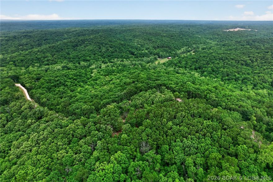 WOW! New Price! 23+ Acres • Creek • Lake Access, Unique earth-contact home on 23+ acres of wooded land with a year-round creek and deeded Lake of the Ozarks access. Ideal for hunting, recreation, or a private rural retreat includes virgin timber. Home offers 3 bedrooms (1 non-conforming) and 1.5 baths with an open-concept layout combining kitchen, living, and family room. Energy-efficient design with low maintenance. Primary suite features private bath with oversized jacuzzi tub. Flexible floor plan allows potential to convert half bath to full and add additional bedrooms. Land is rolling and usable—perfect for hiking, building a shop, garden, or hobby farm. Additional features include private well, gated circular driveway, utility room with washer/dryer and sink, and a 10x20 metal shed with electricity for equipment and storage. Rare opportunity for acreage with creek and lake access.