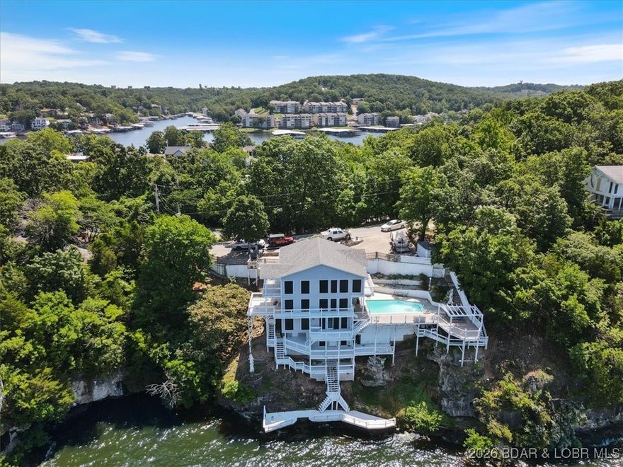 Perched above the shimmering waters of the Lake of the Ozarks, you'll never tire of the fantastic panoramic views. From sunrise coffees on the deck to sunset gatherings by the pool, every moment here feels like a vacation. Centrally located in the heart of Osage Beach, you’ll enjoy quick access to shopping, dining, healthcare, and all the lake activities that make this area such a sought-after destination. Whether you’re searching for a weekend getaway, a full-time residence, or an investment opportunity, this location truly checks all the boxes. Step inside to discover 4 bedrooms and 3.5 baths, second level kitchen, and bottom level bar. The huge master suite is a true sanctuary, with a generous walk-in closet and an elegant en-suite bathroom. Also included, is a built-in storm shelter for peace of mind during inclement weather and access to a community boat dock complete with your own slip! Large windows and sliding glass doors seamlessly connect the indoors to the expansive deck and outdoor entertaining areas. Come experience the unbeatable view, the amenities, and the lifestyle that makes this property so special!