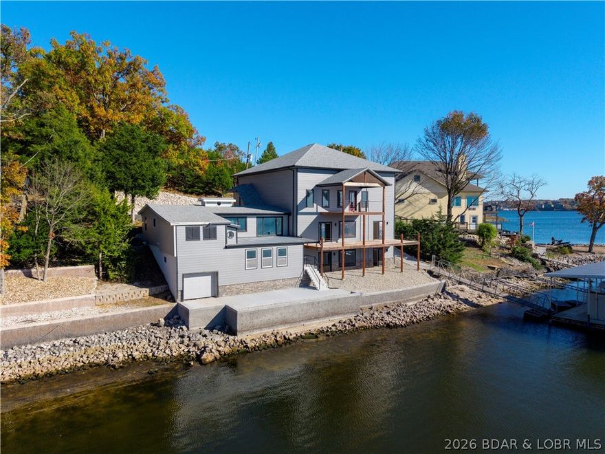 This exceptional main-channel lakefront home includes a rare 1-acre second-tier parcel, adding privacy, flexibility, and long-term value. The standout 1,800 sq ft Hydronic floor heated garage features a 16-ft door, wet bar with refrigerator and dishwasher, loft storage, and ample space for your RV, boat, and lake toys—plus 110 feet of shoreline with a large Ameren permitted dock envelope AND stunning views.
The 5-bedroom, 4.5-bath home captures panoramic water views in both directions. The modern kitchen offers high-end finishes and appliances, while the primary suite features a spa-inspired bath. A custom wine cellar adds character and charm. Three bedrooms and two baths are complete, allowing you to comfortably finish remaining spaces to your taste—ideal for personalization or investment. Short-term rentals are permitted.
Expansive decks showcase unforgettable sunsets, a new seawall protects the shoreline, and pricing reflects the pre-listing inspection and current finishes left to be done, creating an outstanding opportunity to build equity and craft your ideal lake retreat.