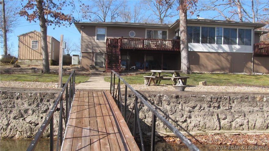 Welcome to your dream lake retreat at the 62 mile marker of Lake of the Ozarks! This well-built, well maintained home offers the perfect blend of comfort, space, & waterfront living. The main level features two full bedrooms & a full bath, along w/a spacious, eat-in kitchen complete w/custom cabinetry, pantry, & stainless steel appliances. The inviting family room showcases a cozy wood-burning stove & opens into an all-season lakeside sunroom—perfect for relaxing & taking in the views year-round. The walkout lower level includes a full bath and a bedroom, ideal for guests, a home office, or additional living space. Step outside to enjoy the lake lifestyle w/minimal steps to your private 2-slip dock, complete w/a swim deck on DEEP WATER  (12-15ft).  Home's additional deck provides the perfect space for grilling and entertaining, and a boat ramp on the property adds extra convenience. This unique property also includes an additional 3.9 acres featuring a barn-shaped garage with two extra garage bays, abundant storage, a half bath, and a carport. A separate entrance leads to a finished party space—ideal for hosting guests or offering potential rental income.