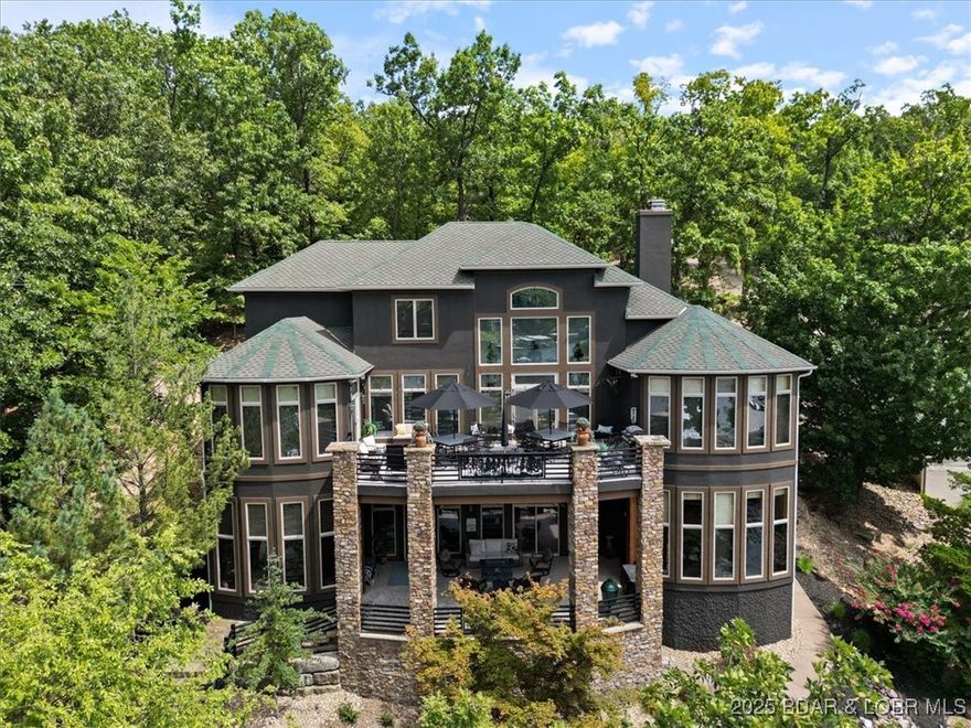 7-BD 5.5 BA Custom One Owner Home with Hand-Hewn Wood Accents, Deep Water and AMAZING DOCK INCLUDED! Landscapping is lush and includes a water feature that leads to the custom 4 well dock w/ hangout space, diving board and high jump latter. This dock would cost $250,000 to recreate! And there is room for a pool in front! This home blends warm rustic charm w/ modern comforts, wood details, warm wood floors, and grand fireplace greet you. Spacious kitchen, Thermador Appliances, granite, rich cabinetry, and ample prep space w/ island, gas stove is a chefs dream. The deck space off the main and lower level allows for gathering year round with room to relax whether you're soaking in the views or enjoying a quiet morning coffee. Upstairs offers 3 BRs of guest space (one with ensuite bath) and a bunk room where kids and cousins make memories to last a lifetime! Family room has box beam ceiling, stone details, custom bar area and 3 more bedrooms! Memberships available Jack Nicklaus Signature golf course, the Club at Porto Cima is a private club with seven waterfront holes overlooking the Lake of the Ozarks. Only 0.9 miles from Grand Point Pool with playground and pickleball courts!