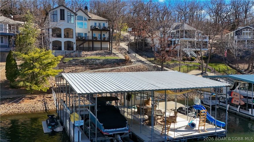 Remarkable turn-key lake home that truly checks every box! Recently updated with thoughtful design and luxury finishes, this home impresses with vaulted ceilings, walls of windows, and stunning lake views. The inviting hearth room flows into a gourmet kitchen featuring high-end appliances, extensive custom cabinetry, and a spacious dining area centered around a beautiful stone fireplace. Lakeside primary suite is a private sanctuary offering a spa-like bath with double vanity, soaking tub, tiled walk-in shower, separate water closet, and a walk-in closet with washer and dryer. The lower level is designed for entertaining with a large family room, full wet bar, lakeside en-suite, three additional bedrooms, 2 full baths, and a separate laundry/storage room. An oversized two-car garage provides space for a golf cart and workshop. Enjoy multiple outdoor living areas including two screened-in decks, one with a hot tub. Cart path leads to the concrete dock, currently configured with a 14x35 slip, with potential to expand to 16’ wide. An additional 18x54 slip can be reopened. Located in a protected cove with main channel views, this property offers excellent access by land and water.