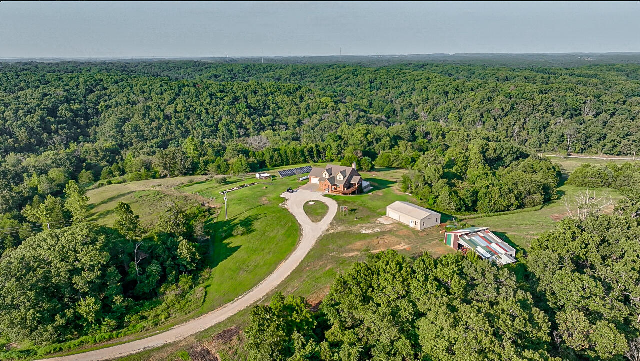 Welcome to Shiloh Hills Farm, a unique retreat nestled on a ridgetop in the picturesque Ozark mountains. This custom-built brick home, set on 51 m/l acres, offers a private sanctuary for those seeking a tranquil lifestyle. The home boasts 5 bedrooms and 5 bathrooms. The primary suite is on the main level and has a spacious walk-through closet. Upstairs, there are 2 bedrooms with their own full bathrooms. Brazilian cherry hardwood floors are on the main level, and oak flooring is on the upper level. In the basement, you'll discover a large kitchenette, perfect for entertaining, and another bedroom with its full bathroom. The tile flooring downstairs adds a touch of elegance and makes cleaning and maintenance a breeze, ensuring your comfort and convenience. The large storm shelter is basement-accessible from the interior of the home. The walkout basement has a large, built-on greenhouse attached to one of the home's exits, making it a desirable area for use. The home has an emergency backup generator and a large solar array. Step outside and discover the possibilities. The property features a large 30x50 shop building with concrete floors and power, perfect for a workshop or storage. Adjacent to the shop, you'll find a spacious barn/animal shelter, offering ample space for your livestock or equestrian needs. The property is perimeter fenced and has many paddocks, making pasture rotation a viable option. There are also ponds and water sources throughout. The Orchard and gardening area lie just out in front of the home. Pastures and woods surround the property in a private setting that offers a great view of the Ozark foothills. With its vast space and versatile features, this property opens up a world of possibilities. Whether you dream of hobby farming or envision an equestrian paradise, this is the perfect canvas for your aspirations.Short drive to either end of Table Rock Lake, Branson, Ozark, Nixa and Springfield.