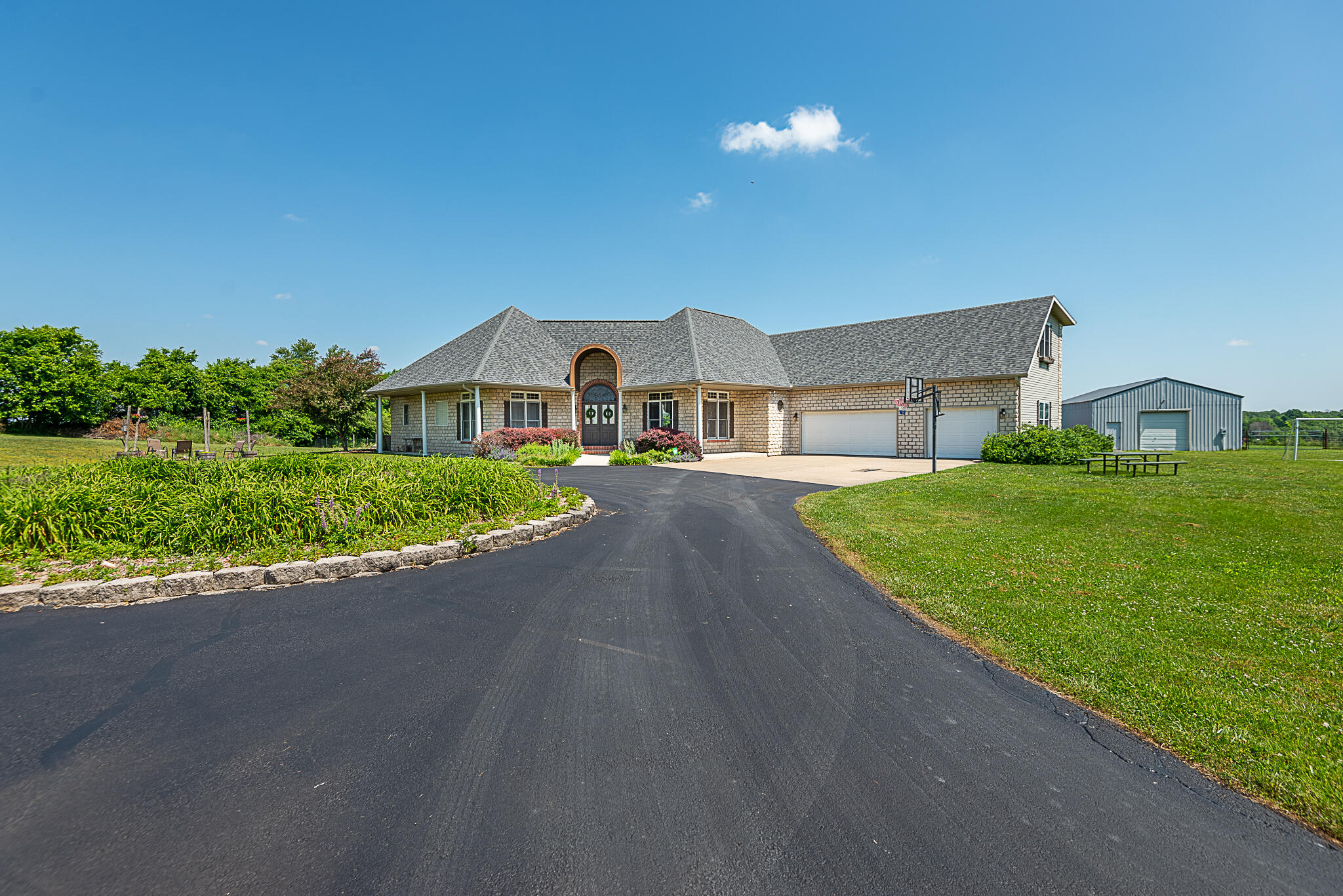 A gorgeous setting and excellent location highlight this hard-to-find family home on approximately 5 acres located just east of Springfield in Rogersville.  With over 3400 sq.ft. of living area, this 4 bedroom, 3 and a half bath story and a half home has room to spare including multiple living areas, formal dining, an open cook's kitchen and a full master suite.  Sitting at the end of a private drive, the setting is private but open with an asphalt circle drive, mature landscaping, basketball and volleyball courts, a full garden area, above-ground pool, and a hot tub as well.  The acreage is very open with great views to the north.  The 25x40 detached shop has a gravel floor and power.  There is also a 14x24 barn currently used as a chicken coop.  The property is cross-fenced as well.  Inside, the living room has a sunken floor with Terra Cotta tile walkways around it leading into the kitchen and dining area with granite countertops, a full island, and stainless appliances, and a nice pantry area. The family room, a full laundry area, the half bath and formal dining are off the kitchen.  The family room has a wood ceiling and exposed wood beams along with a brick wood fireplace as it's centerpiece.  The stairs lead up to 2 large bedrooms with a full bath over the 3 car garage.  The master suite and 4th guest bedroom are on the west wing with a den area leading into the master suite with double vanities, a large walk-in closet and shower area.  Updates and other features includee a newer roof, lighting and plumbing fixtures, geothermal heating and cooling, central vac, and so much more.   Super convenient to Rogersville or Springfield and is in the solid Rogersville school district too.  This stunning home is perfect for the growing family looking for country living at it's best without the remote location.