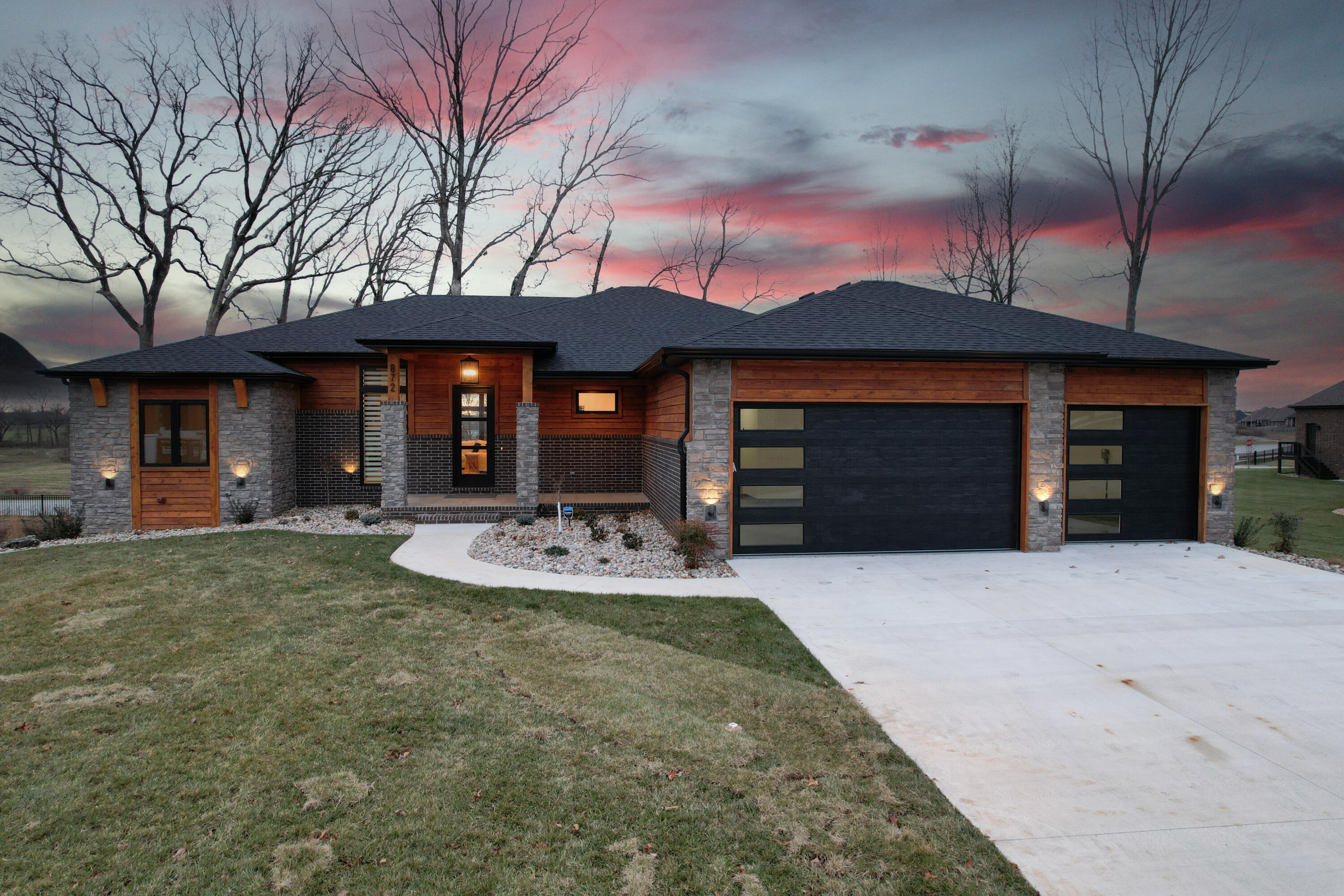 Exquisite, new home built in 2023 in The Estates of Enniskerry, Wicklow's popular gated community in Nixa, MO.  This spectacular walk-out basement home with a modern flair features approximately 5,169 total square with 4,529 square feet of finished living space w/ 5 bedrooms, 4.5 baths, multiple living spaces and a 3-car garage with epoxy flooring.    From the moment you step into the elegant entry with an iron staircase, you will enjoy an open-concept living space with lots of natural light.  The dramatic, shiplap, gas-log fireplace, black windows with custom window treatments, and luxury vinyl plank flooring found throughout the home sets the stage for both elegance and casual comfort.   The magnificent kitchen features a large center island, quartz countertops, a sleek backsplash & cabinet color combination, stainless steel appliances, including a gas cooktop with a decorative hood, a wall oven & microwave, a dishwasher, and a refrigerator plus a spacious walk-in pantry to die for!   The under-counter and upper glass cabinetry lighting creates a warm ambiance for evenings at home, where you will LOVE relaxing in the magnificent, main-floor master suite!  The master bath with dual vanities, soaking tub & walk-in tile shower connects to a huge walk-in closet, connecting to the large laundry room with sink & lots of cabinets for storage.   There is also a convenient mud room with bench & more storage opportunities for the family.  The main floor also offers a spacious dining area, a covered, screened-in porch with composite flooring, and two additional ensuite bedrooms.   Downstairs, there is a large living/rec room complete with a 2nd gas-log fireplace, a stylish wet bar, media room, two additional bedrooms & bath, a finished John Deere room, unfinished storage & storm shelter.  The amenities go on and on...and you're sure to enjoy the security of the gated community with amenities including two swimming pools, tennis courts & more!   Call to schedule a showing!