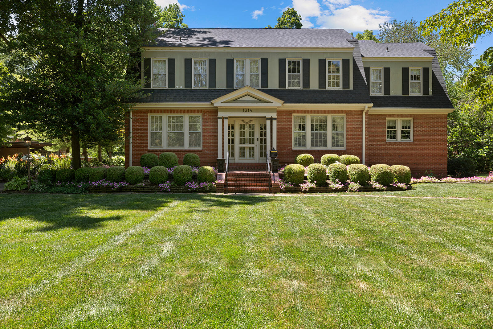 Discover 1314 East Walnut Street, a timeless masterpiece crafted circa 1930s in the American Colonial Revival style by A. M. Curtis. This historic gem, built on the site of the George McCann farmhouse, seamlessly blends original character with contemporary comforts. Ideal for entertaining, the main floor showcases a large living room with beamed ceilings, cedar mantel surround, stone accents, and pegged hardwood flooring. A sun parlor and formal dining room open via French doors, while an updated kitchen boasts commercial-grade appliances, granite countertops, and a pantry. Adjacent, a half bath offers convenience. Boasting five spacious bedrooms, including a second-floor laundry room (4th bedroom), this residence offers sanctuary. The primary bedroom features an en suite bathroom with a stunning shower, luxurious soaking tub, granite double sinks, and ample closet space, including a walk-in with built-ins. A sun parlor extends the primary suite, leading to a charming balcony. The second floor is designed with a coffee bar, multiple closets with pull-out drawers, and a laundry shoot. Generous secondary bedrooms include a third bedroom with a unique rounded doorway, adjoining a character-rich bathroom. The oversized fifth bedroom preserves historic charm with an en suite bathroom and walk-in closet. Original details like an impressive staircase, storage closets, crown molding, and glass door knobs enrich the home, complemented by a secondary staircase to the two-car garage. Outside, the 0.83-acre lot features lush gardens and ample entertaining space. The brick and stucco exterior, with a second-floor balcony, enhances the home's timeless appeal. Experience the blend of historic charm and modern luxury at 1314 East Walnut Street--an opportunity not to be missed.