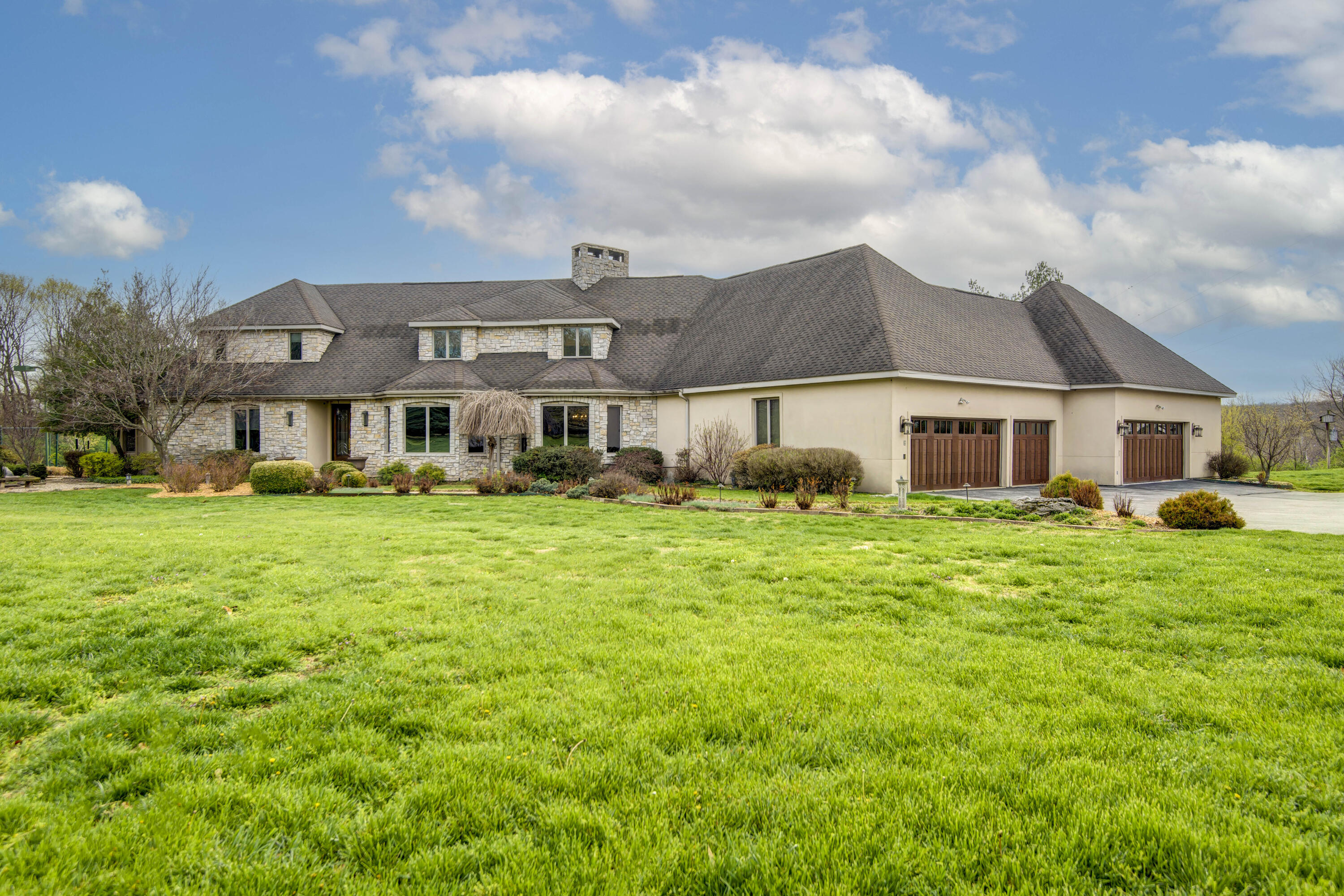 'Relax and Entertain' should be the mantra of this magnificent estate home in Southeast Springfield.  This 8,000 square foot home is situated on 4.28 acres adjacent to Natural Bridge Estates and across from the Terraces.  You can't find acreage like this in town and be any closer to hospitals, schools, shopping and restaurants.  Relax with friends and family on the spacious, covered patio with an incredible outdoor kitchen, raised ceilings and fantastic rolling hillside views.  The outdoor kitchen has a wood-fired pizza oven, Green Egg, Evo, and smoker.  Steps away from the patio is the expansive pool deck where you can enjoy the outdoor fireplace and views of the James River Valley.  Additionally, there are meditation gardens with a Koi pond, pergola and flower beds galore.  Entertain your guests in the fun recreation room with a pool table and bar, or watch a movie in the home theatre.  Afterwards, retreat out back to play tennis (tournament lighted), bocce ball or pickle ball.  Take some time for yourself and get lost in the home art studio, or in the yoga/meditation room, or garden in the green house and prepared garden beds.