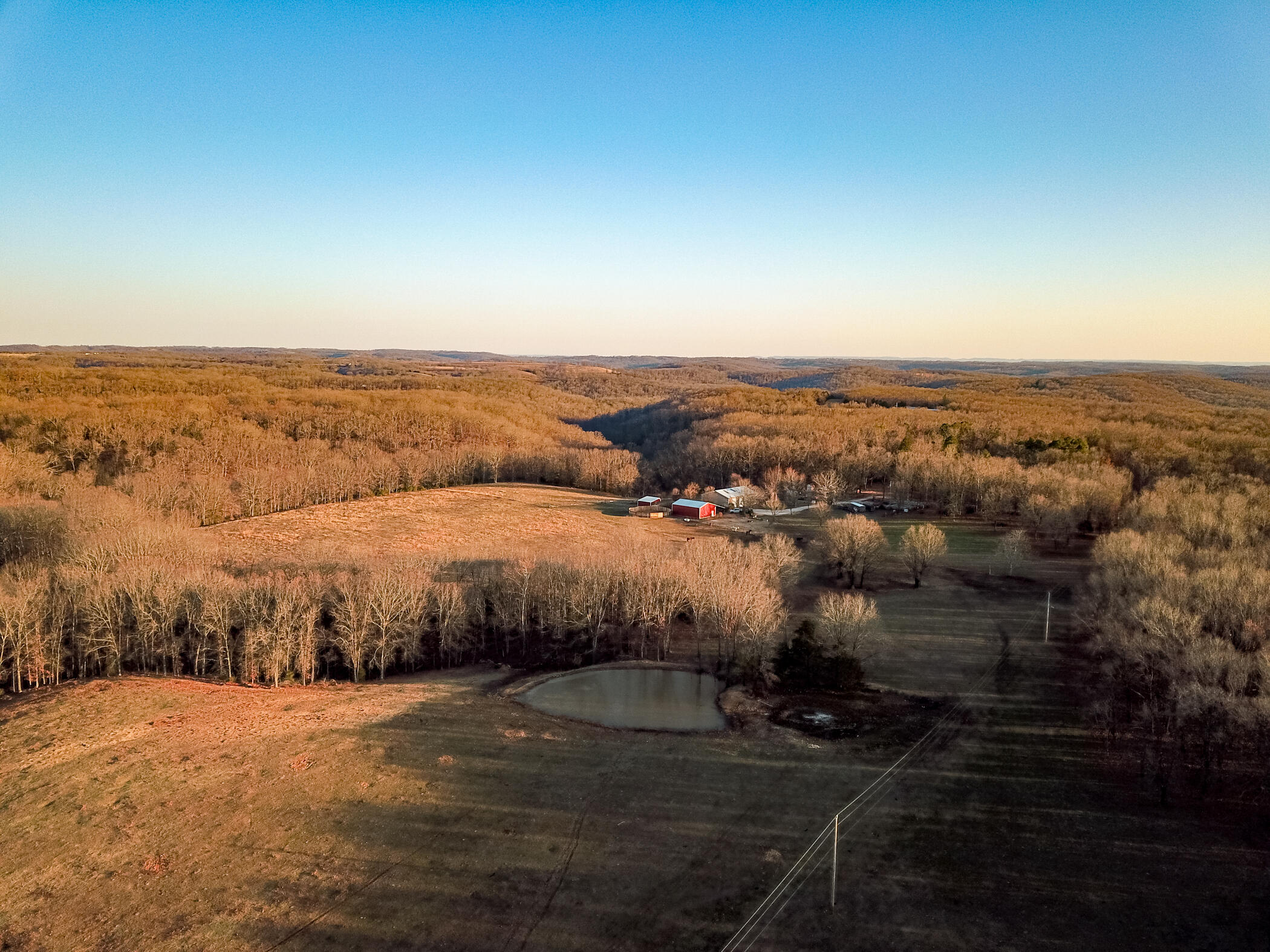 This 107 acre southern Missouri tract features a nice balance of pasture and timber, well-planned and well-built livestock facilities, living quarters with plenty of storage and outbuildings, good highway access, and a private home setting, all within an easy drive of town. The centerpiece is the farmstead, situated 1/2 mile down a private lane. Here you'll find a 2,400 s.f. barndominium with half of the area devoted to living space and the remainder to shop space. The living space features an open living/dining/kitchen area. Two bedrooms and a roomy bathroom are located down a short hallway, with a laundry room between. Exterior doors open onto all three sides of the wrap-around porch. If the 1,200 s.f. of living space isn't quite enough to meet your needs, take comfort knowing that there's another 1,200 s.f. of loft space that could readily provide the additional room your family might require. This farm was designed and built to handle livestock efficiently. A 30'x40' hay barn w/ 18' lean-to offers plenty of space to store equipment and forage. Other outbuildings include a 20'x20' calf shed, 12'x12' well house w/ loft, 10'x14' greenhouse, and an 18'x30' enclosed carport. Livestock handling is made efficient through the use of welded pipe corrals, sorting pens, and cattle chute w/ newer headgate. Horsemen will appreciate the five horse paddocks, 50' diameter round pen with solid sides, and numerous gates operable from horseback. The farm is set up for self-sufficient living, ready for cattle, horses, sheep, goats, and hogs. A chicken coop is near the house, along with the greenhouse and multiple raised garden beds. Firewood and forest products are plentiful in the oak covered ridges and valleys located east of the homestead, and the owners have spent many hours engaged in timber stand improvement to foster a healthy forest. An old wagon trail meanders through the woods, passing near a permanent spring that produces an estimated 50 gallons/minute.