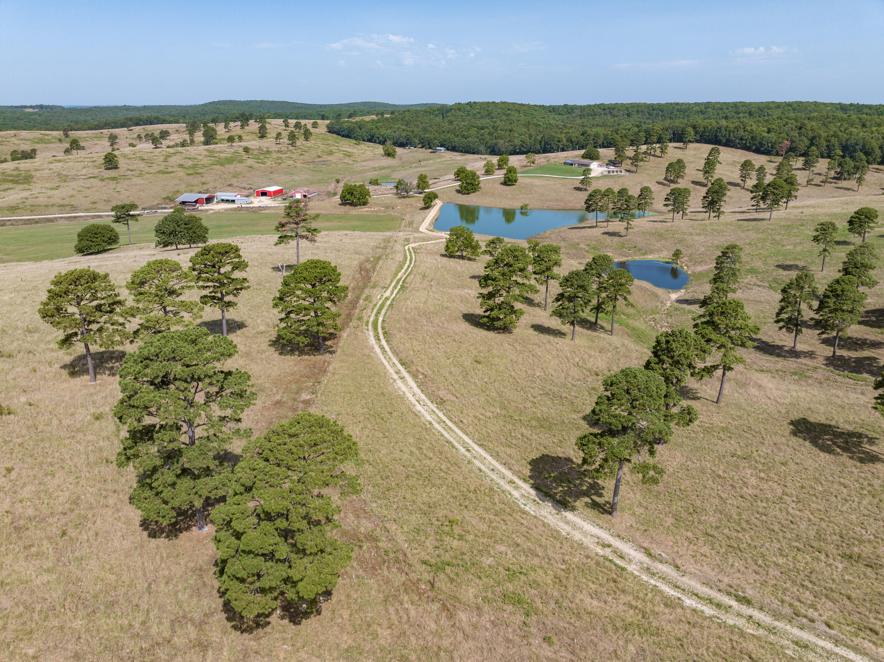This 1753 +/- acre property is conveniently located just off Highway N north of Gainesville. The property offers approximately 750 acres of open pastures with great views in all directions as well as approximately 1000 acres of mature timber with trails, springs and food plot areas for recreation and hunting.  The 4 beds, 3 bath earth-berm home built in 1993 is 1.1 miles off the highway and sits high on a hill and overlooks most of the property.  The home offers a large open kitchen, formal dining room, walk-in closets, large 2-car garage and so much more. The home is serviced by dual fuel heating with both electric and an outdoor wood furnace.  Barns and outbuildings include a 48x70 red iron equipment building built in 2020, 44x70 with 24' overhangs on both sides commodity building built in 2010, 50x60 with 16' overhangs on side and rear insulated shop with concrete floors and LP and wood heat, 2 livestock barns with cattle working systems and pipe corrals, 34x 104 hay barn and 24x 70 equipment barn. North of the main buildings is a sow farrowing barn with slatted floors and 16 farrowing crates.  Most of the fencing has been done since 2005 with the oldest stretch being built in 1995. The fencing and cross-fencing is 5 strand barb wire mostly with pipe corners and have been designed for easy flow of cattle from the corrals to all pastures by one person.  The property has multiple ponds and lakes as well as automatic waterers for ample water for livestock.  The wooded portion of the property is a hunter's paradise with cleared trails throughout.  There are a multitude of food plot areas as well as places to build a cabin.  The east side offers a 3-level spring that is over 20' tall and flows year-round. This property offers opportunity for several different applications and is a must see.