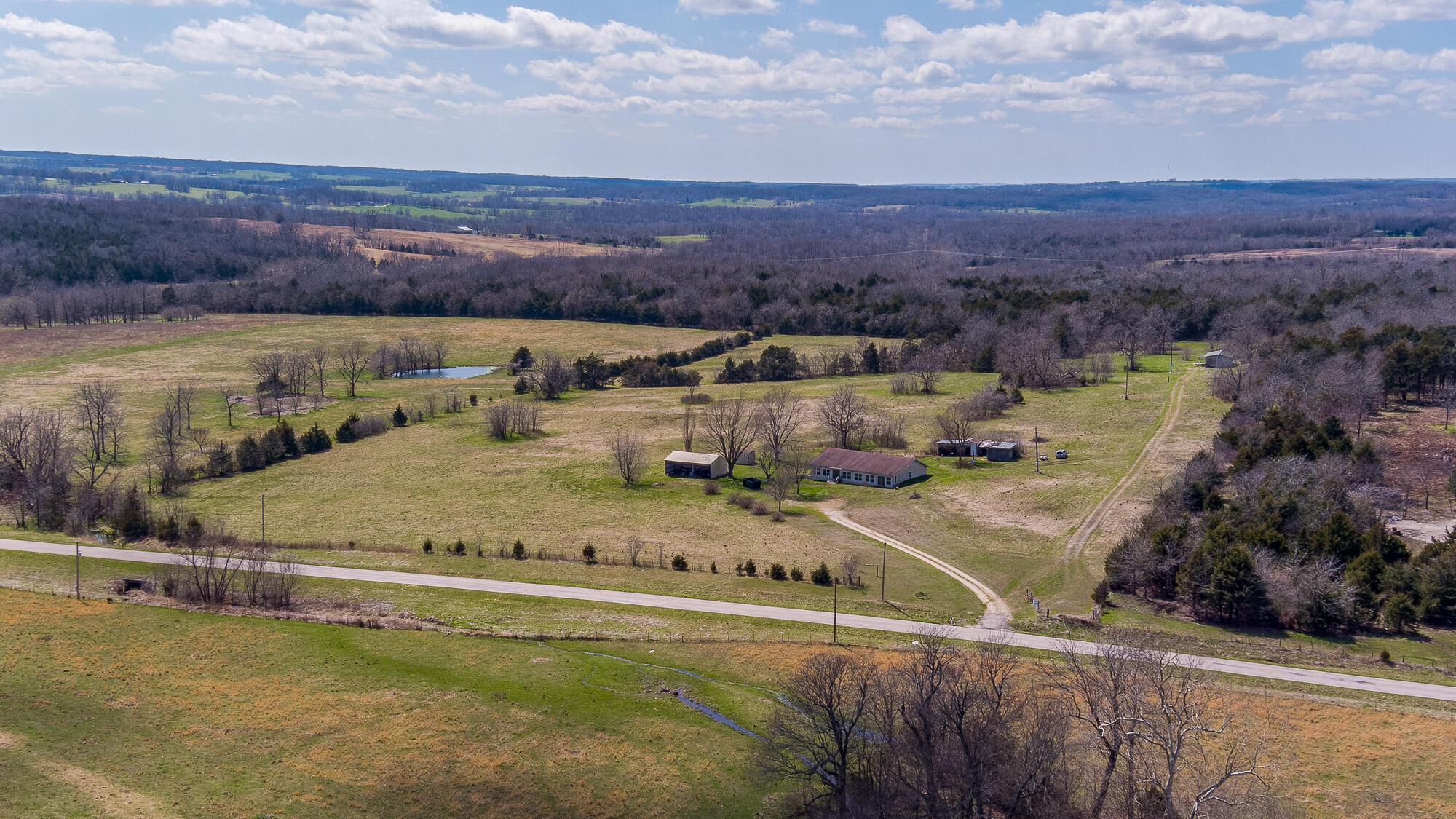 Nothing eases the mind quite like a sprawling country view from the peace of your front porch, and with this home and 19.5 acres, you'll have a front row seat to some of the best sunrises Southwest Missouri has to offer. Enjoy a cup of coffee from the large enclosed front porch, or gather friends and family around a farmhouse table in the spacious kitchen/dining area. Hunt to your heart's content on prime hunting ground within walking distance of your home. The 2,100 sqft home boasts 3 large bedrooms with walk-in closets, a walk-in pantry, three bathrooms, and the panoramic view is also accessible from the comfort of your couch, as the living room has large glass doors leading back to the enclosed porch. When it's time to enjoy the outdoors, there's a large machine shed and two outbuildings. The property is truly a sight to see for yourself. Secure your view of a county line sunrise and schedule a viewing today!