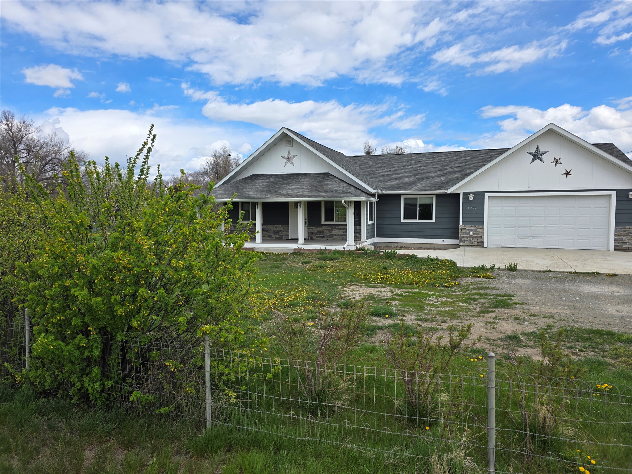 View of front facade with a shingled roof, an attached garage, covered porch, stone siding, and driveway