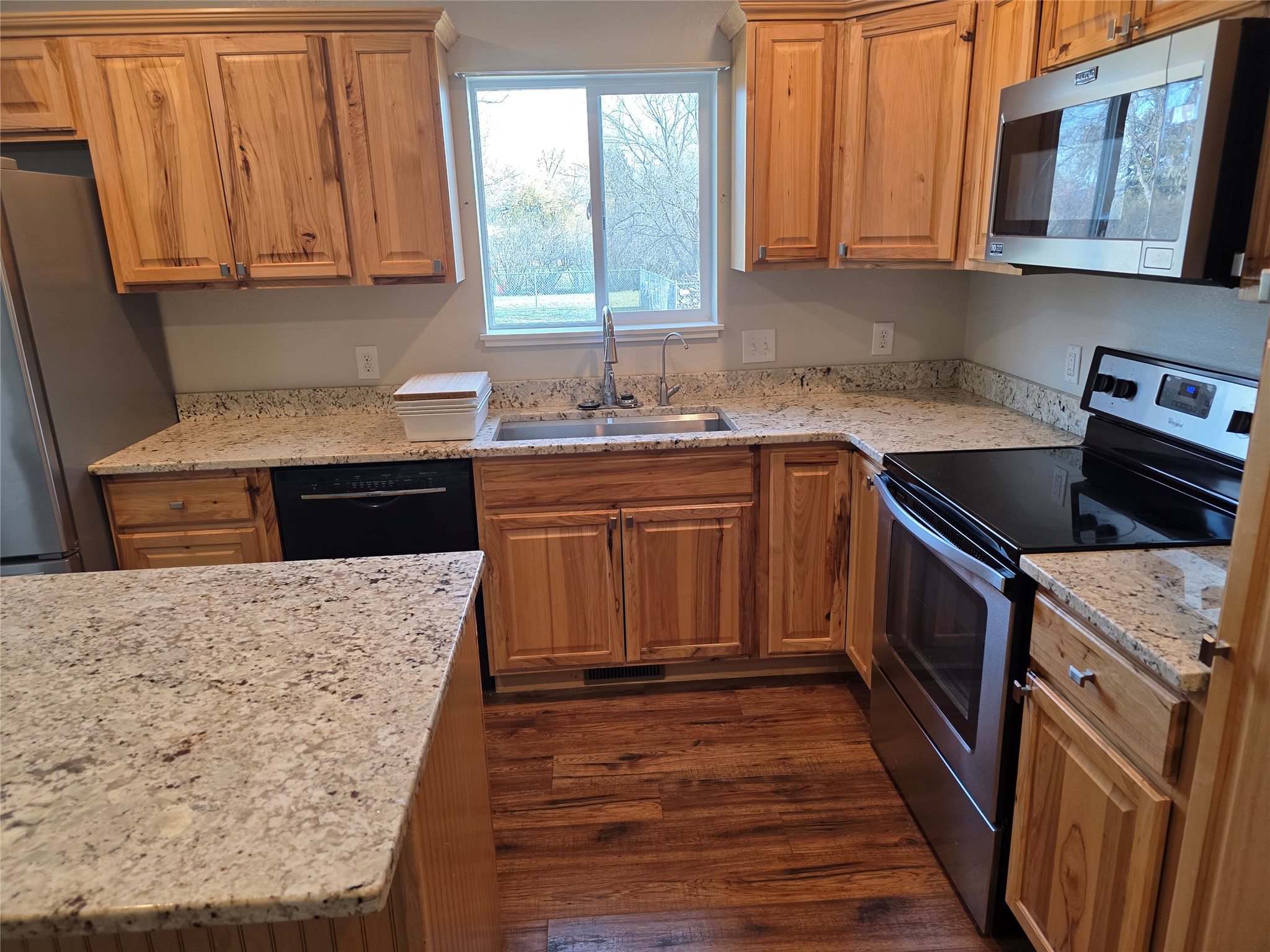 Kitchen featuring appliances with stainless steel finishes, dark wood-type flooring, light stone counters, and brown cabinetry