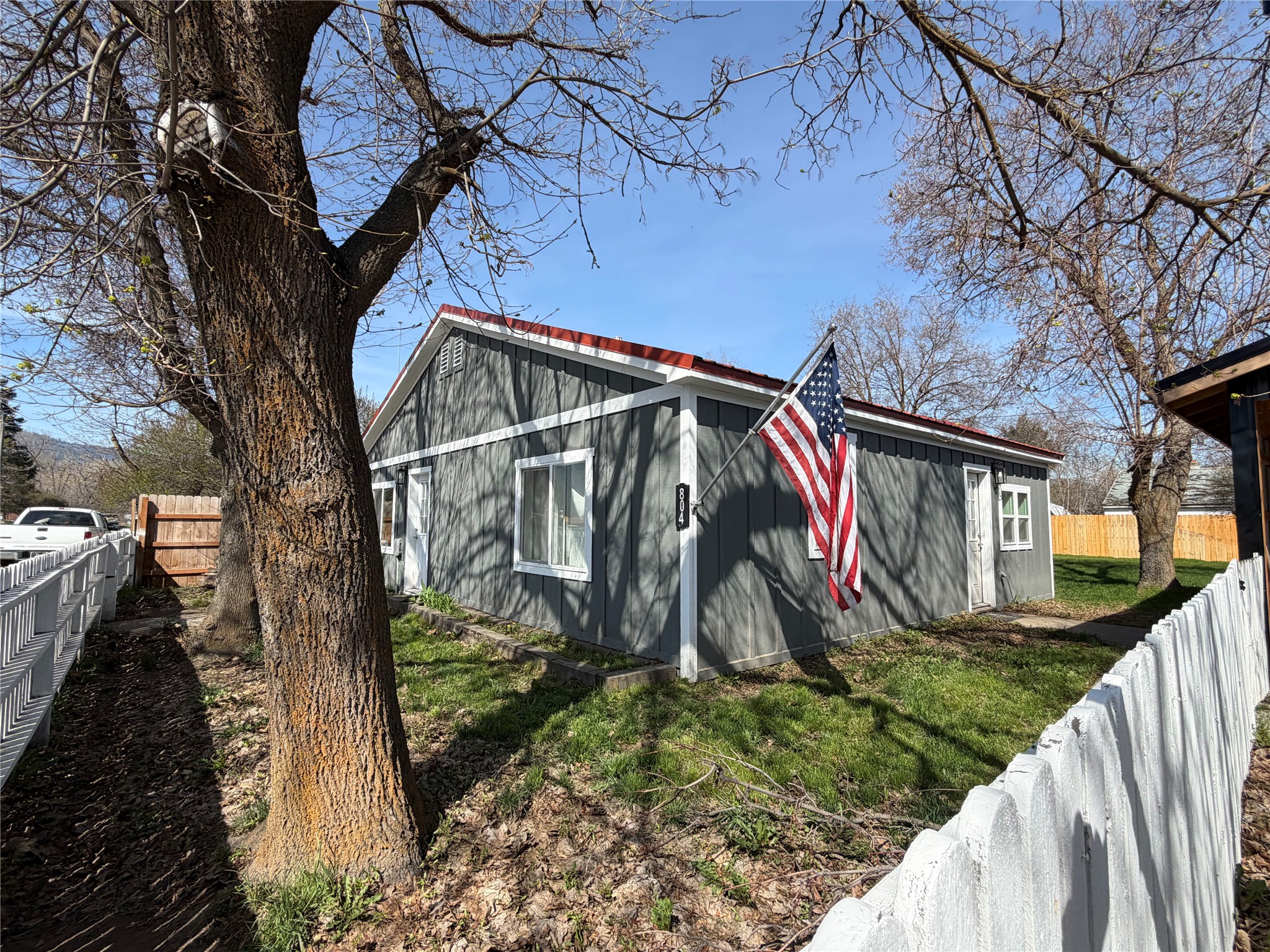 The property features a gray exterior with white trim, a red roof, and a white picket fence