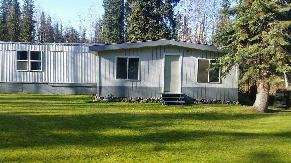 Gray single-story home with front steps and a broad lawn, surrounded by trees.