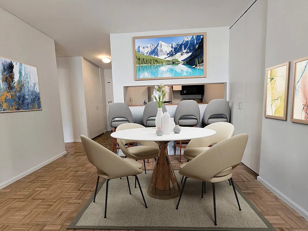 Dining area with a round white table, upholstered chairs, parquet flooring, and framed artwork.