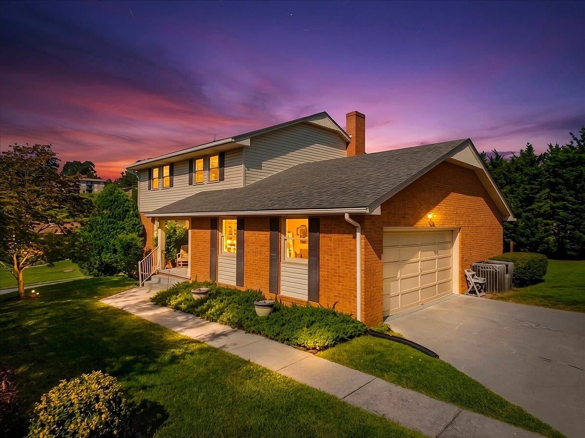 Two-story brick and gray-sided home with a large garage, lit windows, and a purple dusk sky.