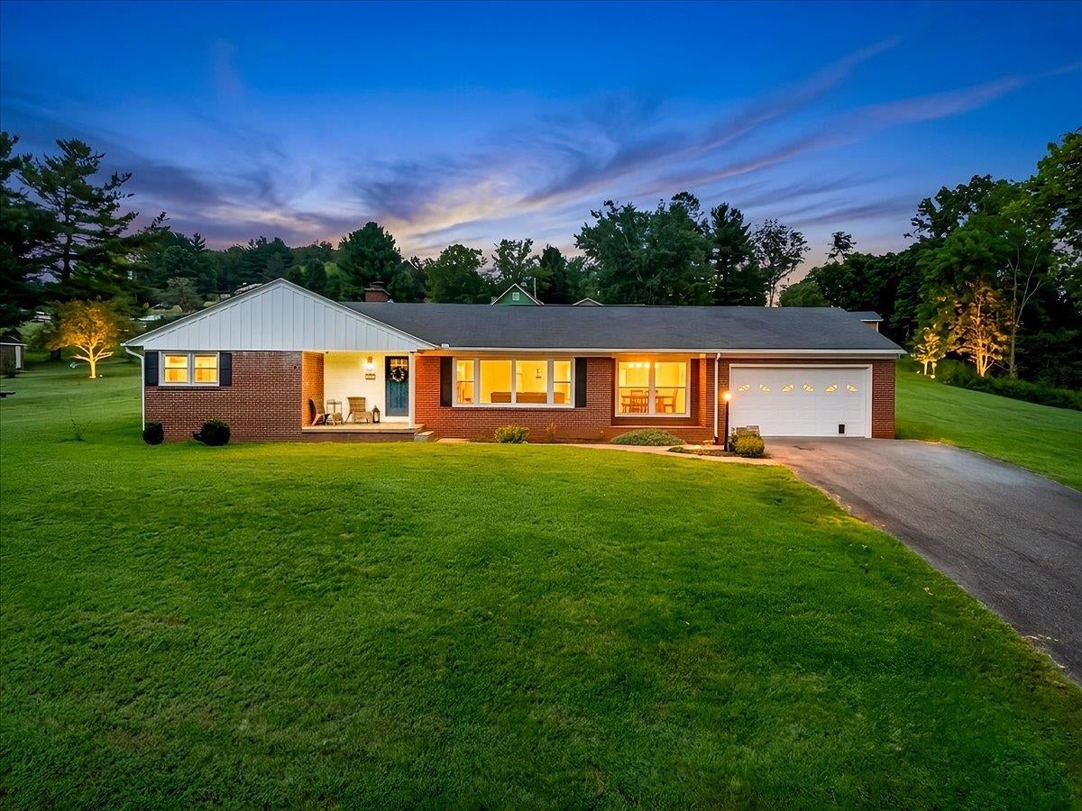 Brick ranch home with a white garage and broad lawn, warmly lit at dusk.
