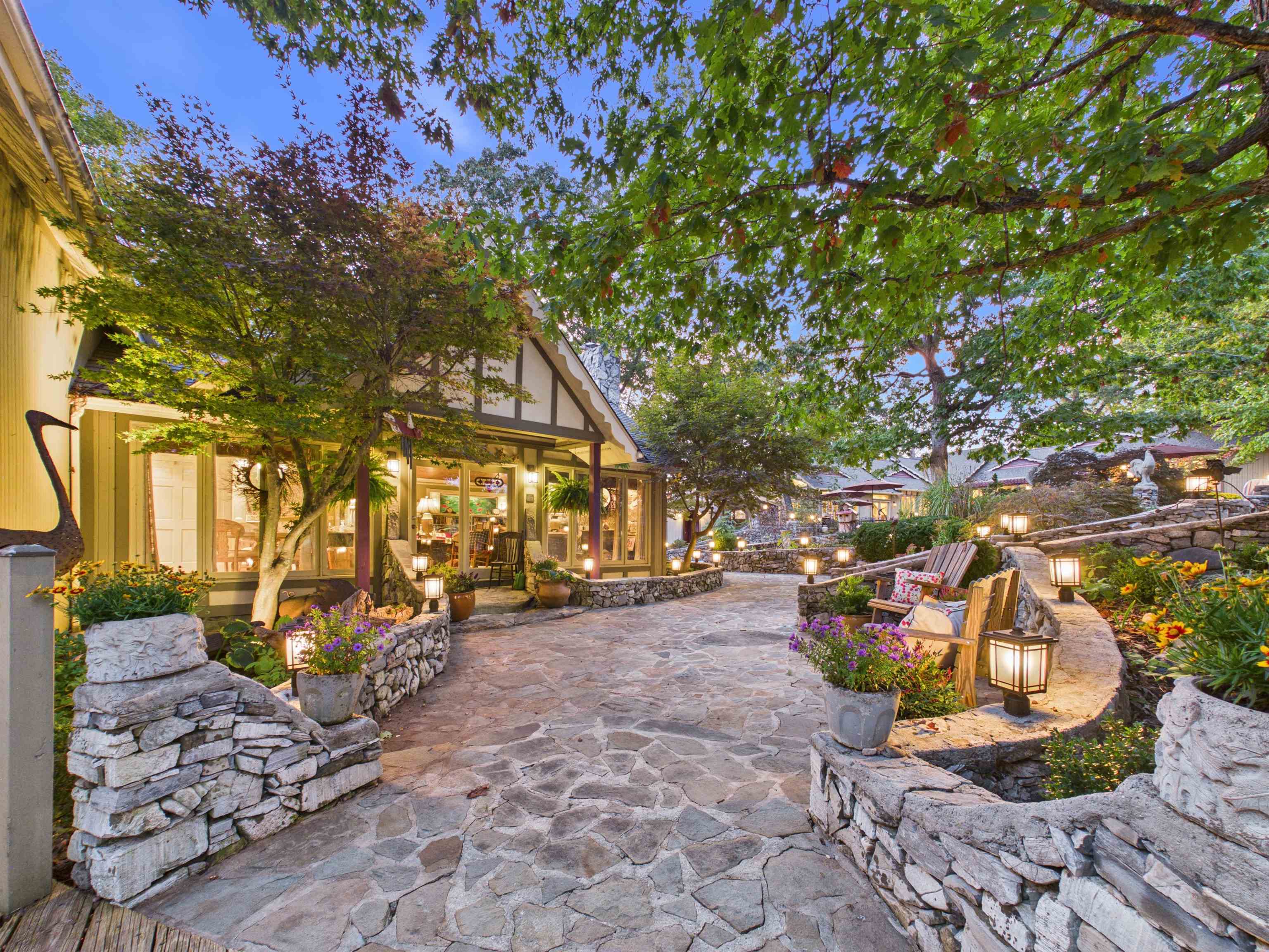 Flagstone walkway through a leafy shopping courtyard with timbered storefronts and stone seating walls.