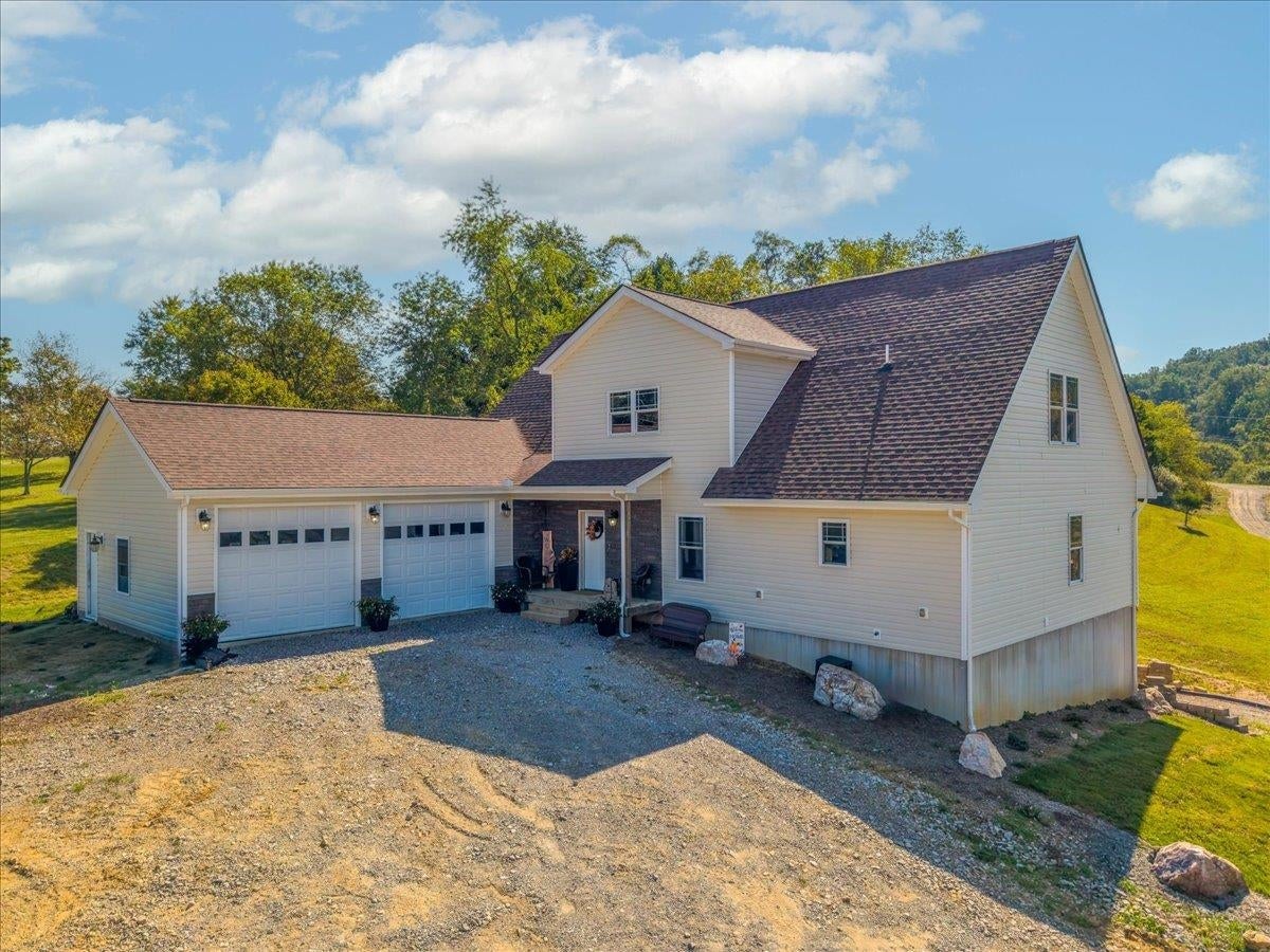 White rural home with a steep roof, attached two-car garage, and broad gravel driveway.