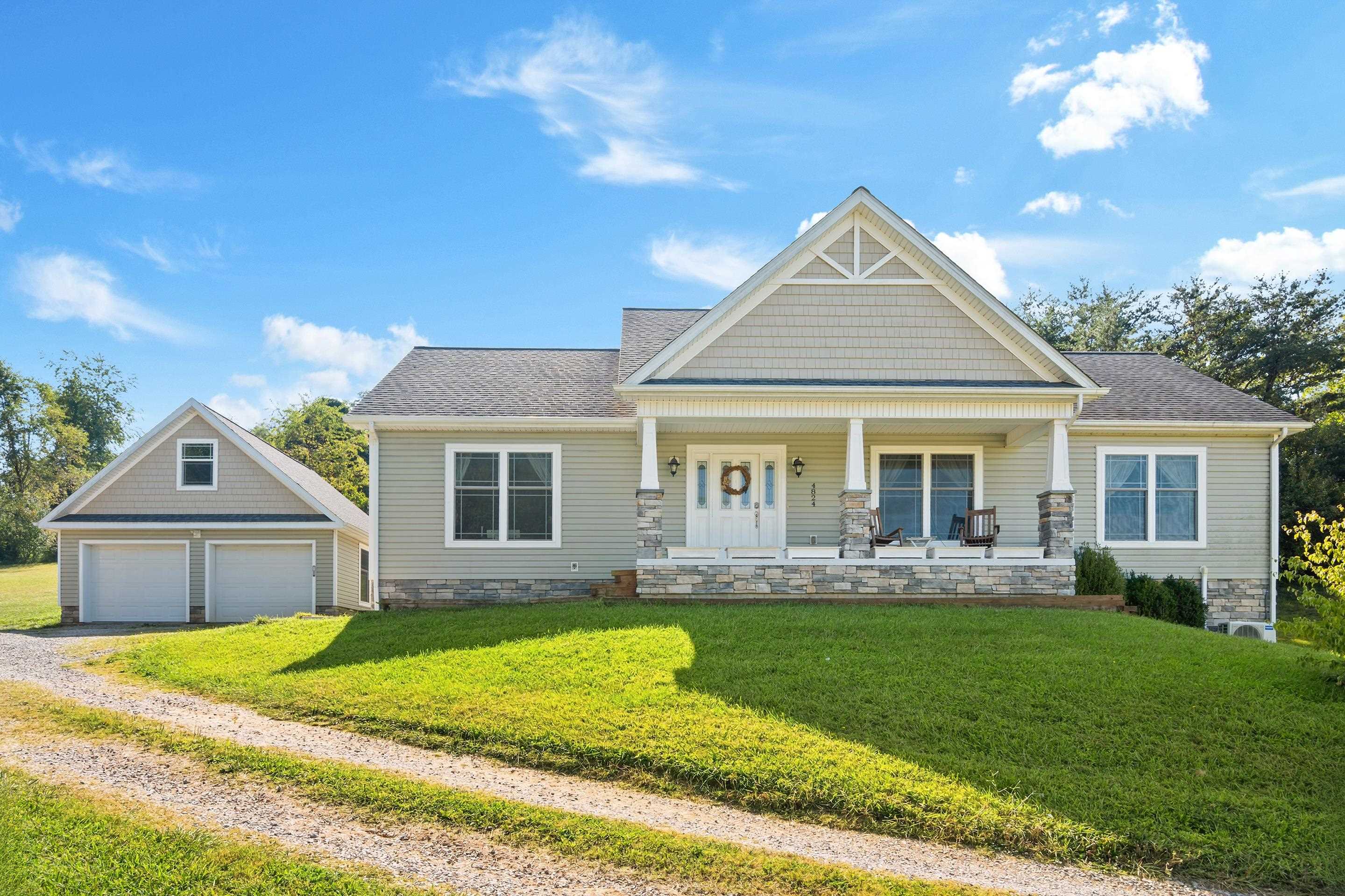 Light-colored single-story home with a covered porch, stone accents, and a detached two-car garage.