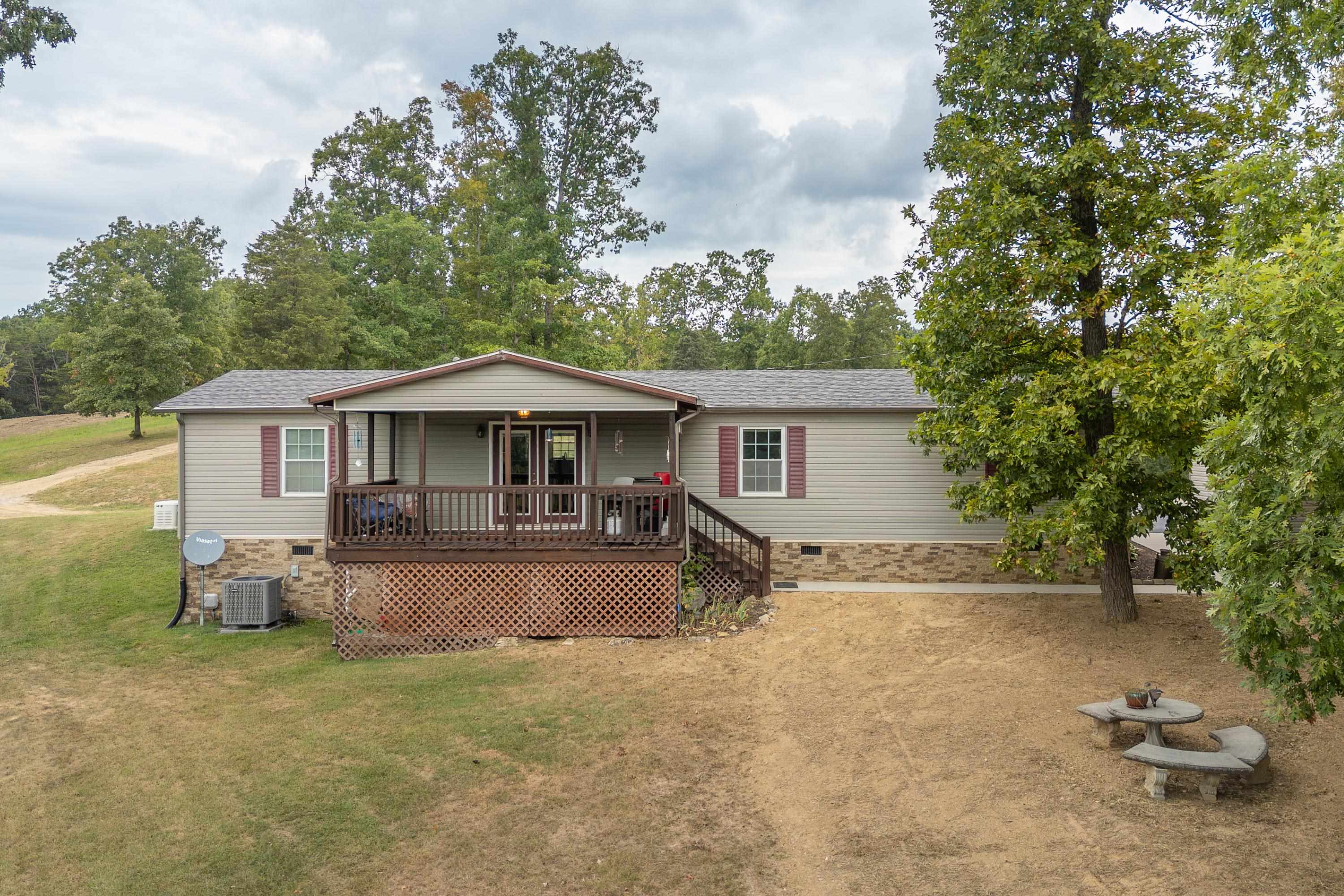 Single-story home with a covered wooden porch, lattice skirting, and mature trees in the yard.