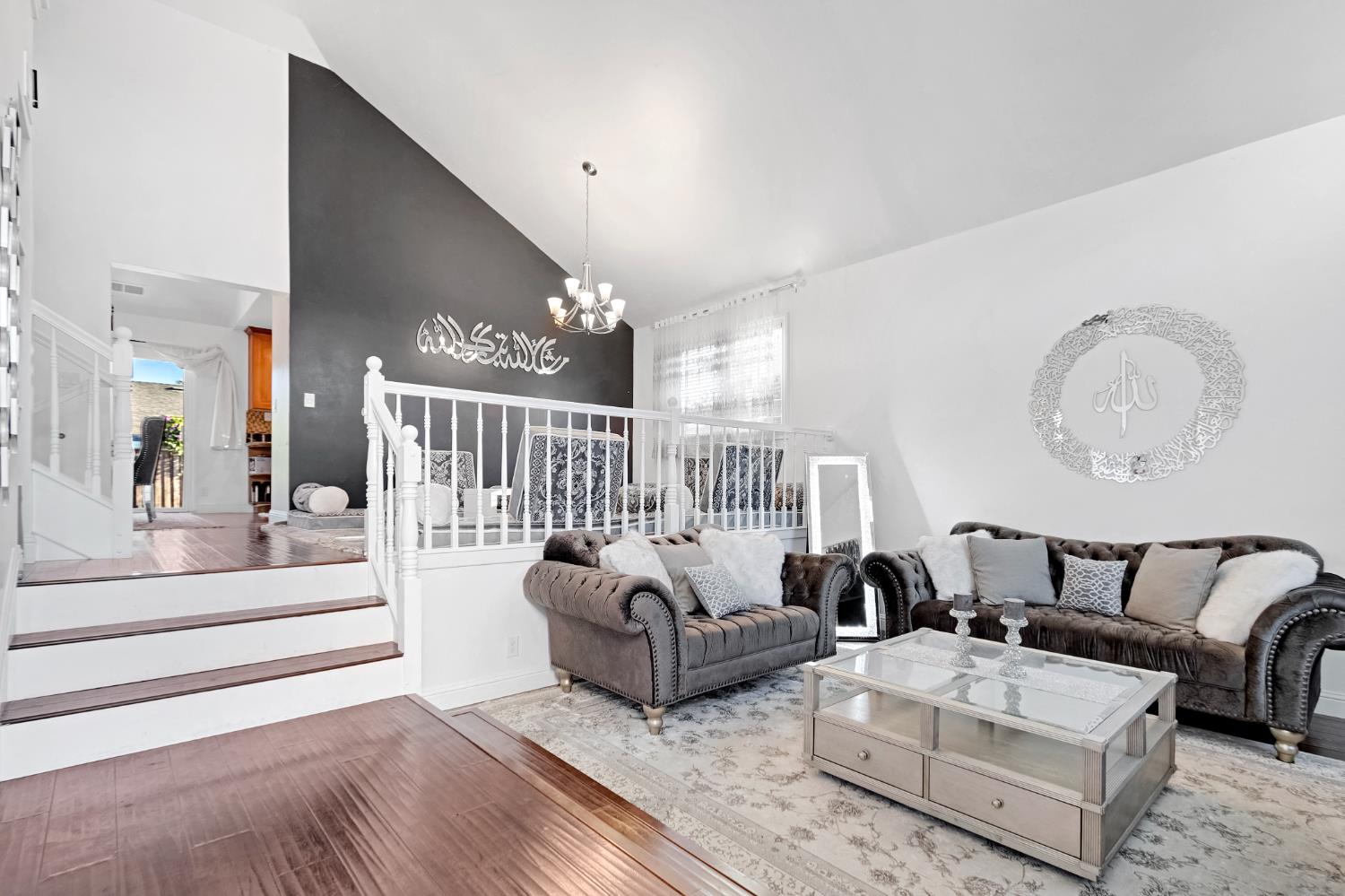 High vaulted ceiling with a contemporary chandelier, rich wood-finish flooring, and white painted balusters