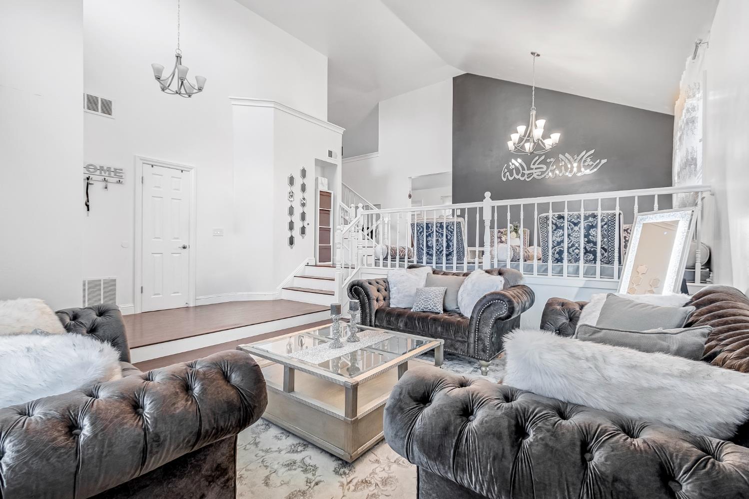 Formal Living room. Soaring ceilings with crown molding, elevated entryway with wood-finish flooring, staircase with white railing, and a modern chandelier
