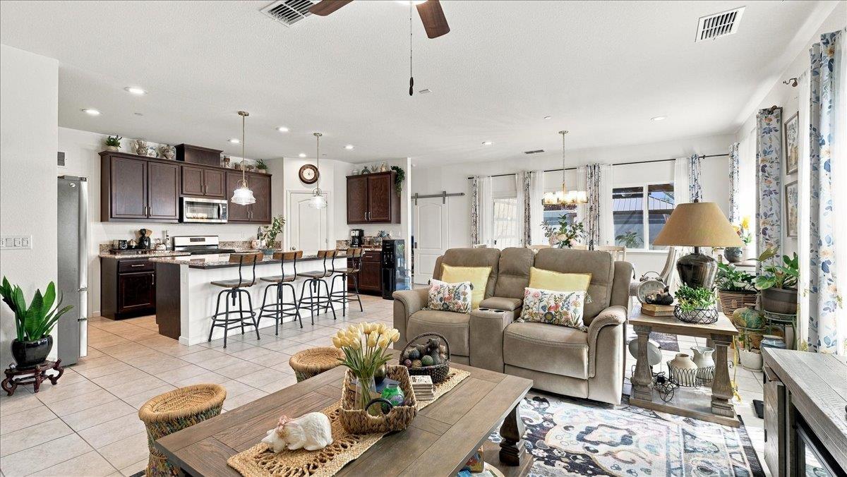 Open-plan kitchen and living room with a breakfast bar, reclining sofa, and large windows.