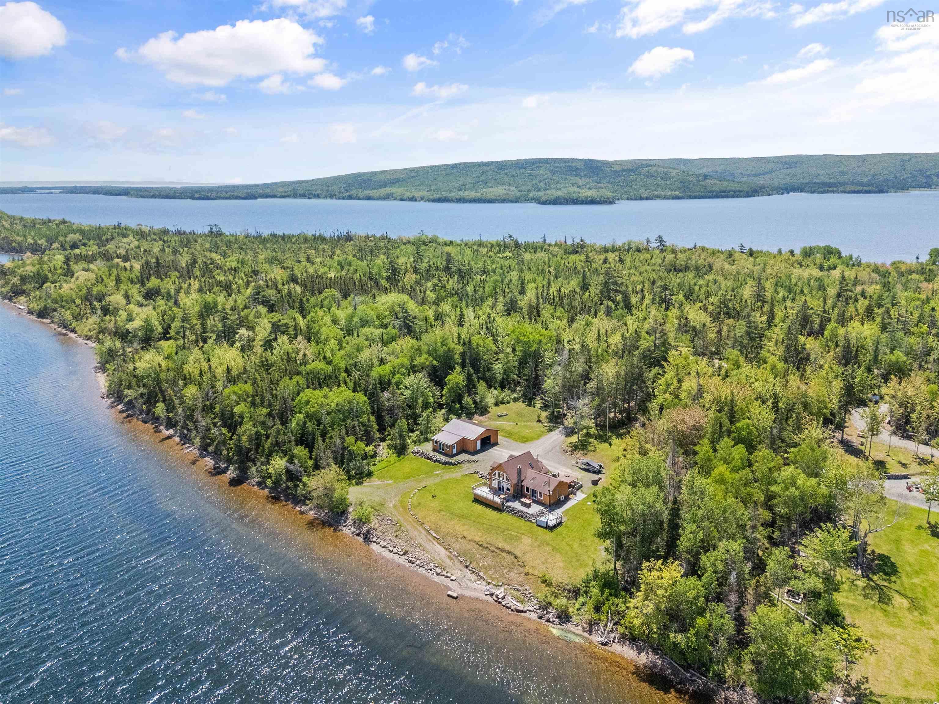 Waterfront property featuring a main residence with extensive decking, a secondary outbuilding, and a forested landscape
