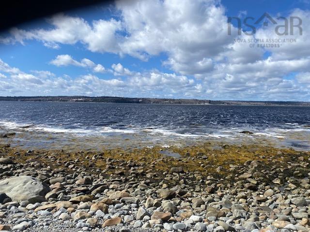 The property is located on a rocky shoreline with views of a wide expanse of water, and a tree-lined distant shore