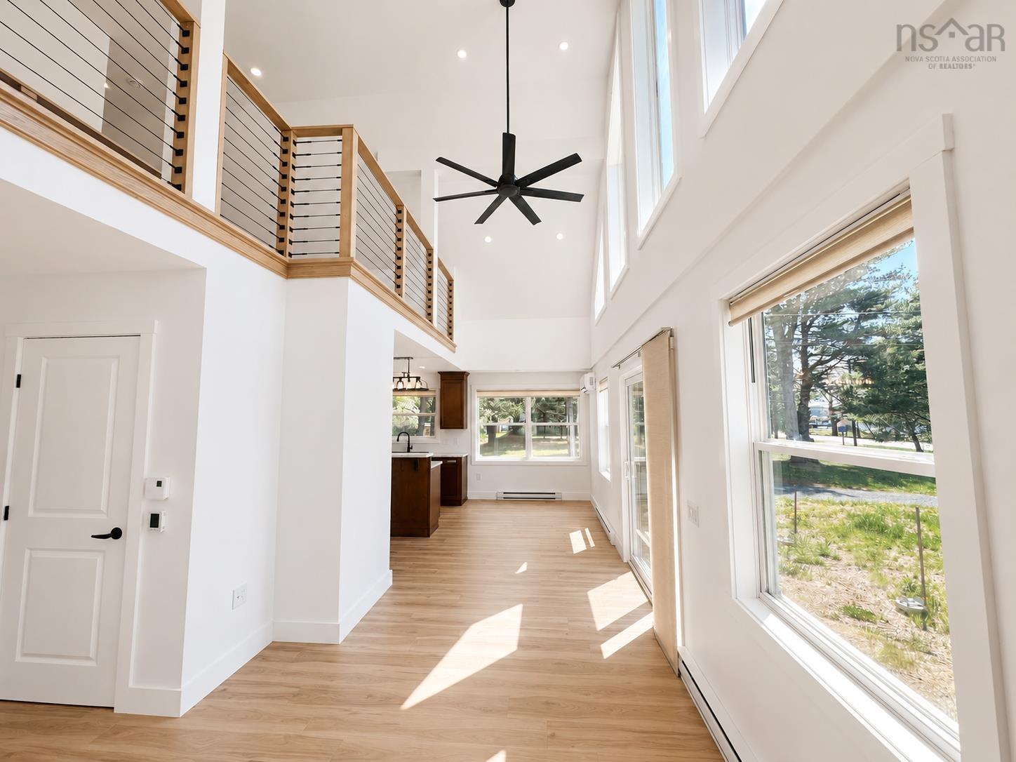 Vaulted ceiling with a contemporary black ceiling fan, wood-finish flooring, and a second-story interior balcony with wood and cable railing