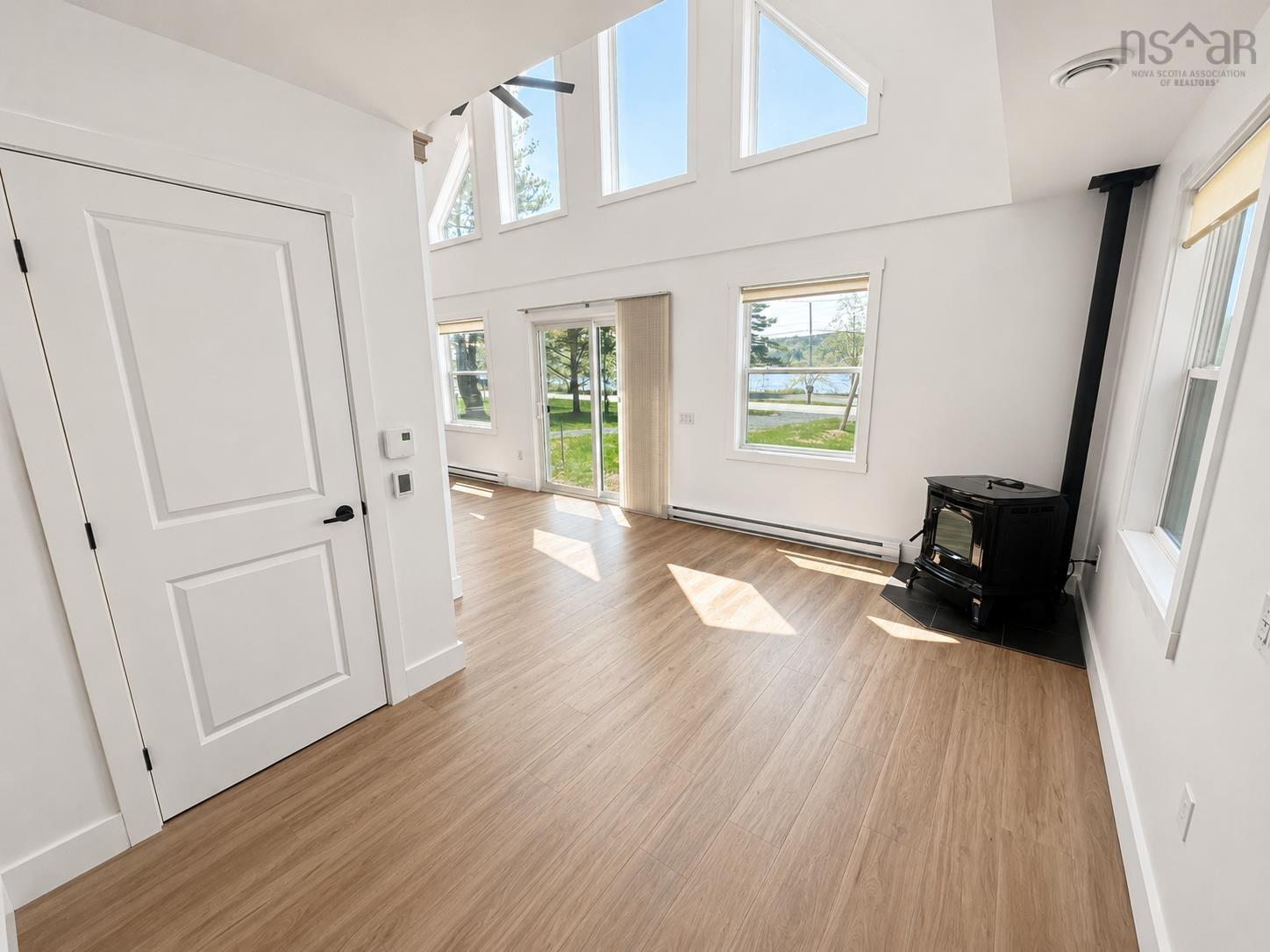 Bright interior space featuring a freestanding stove, high vaulted ceiling, and wood-finish flooring