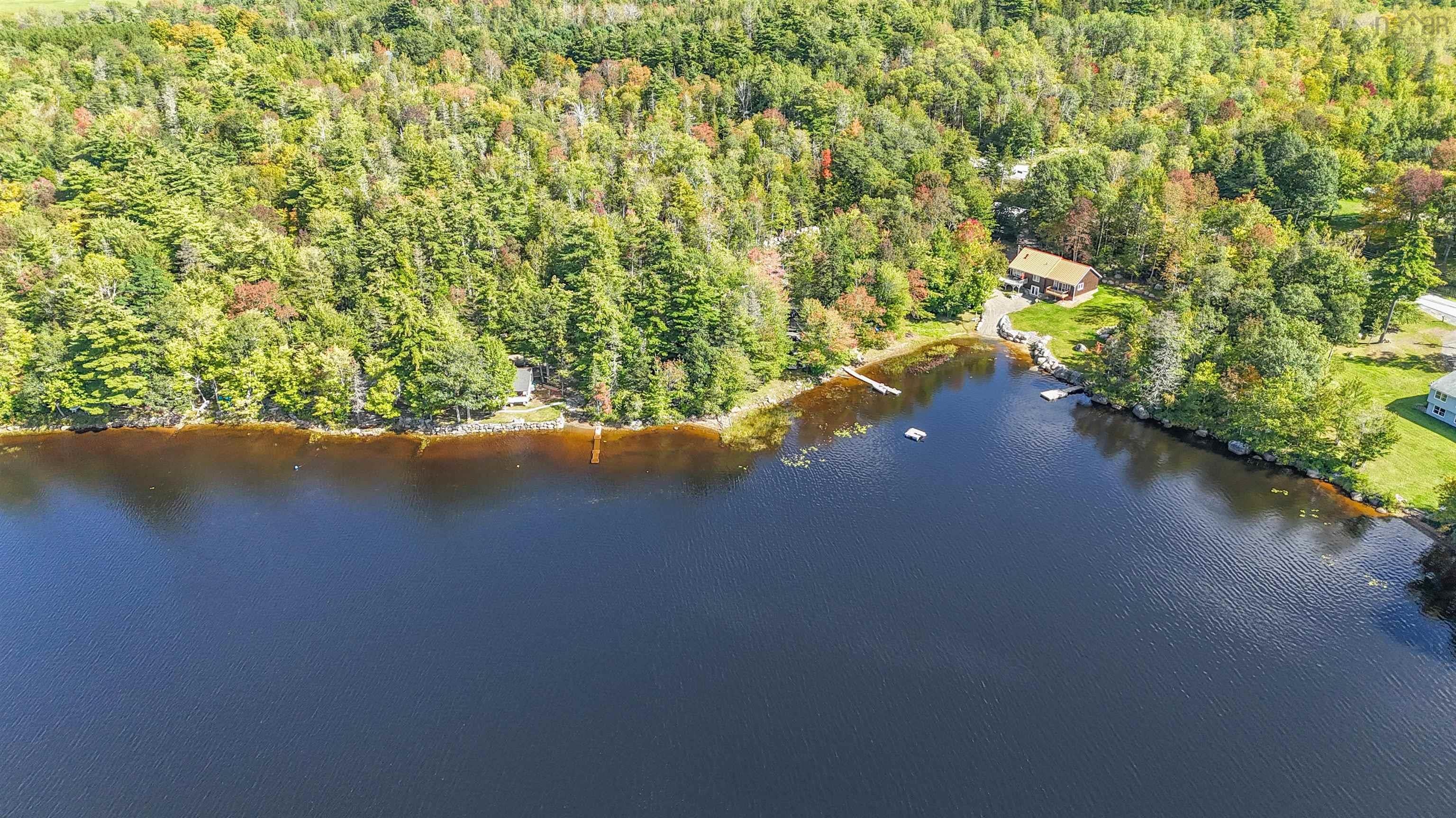 Expansive lawn with natural rock features, mature trees, and waterfront access to a calm body of water with docks