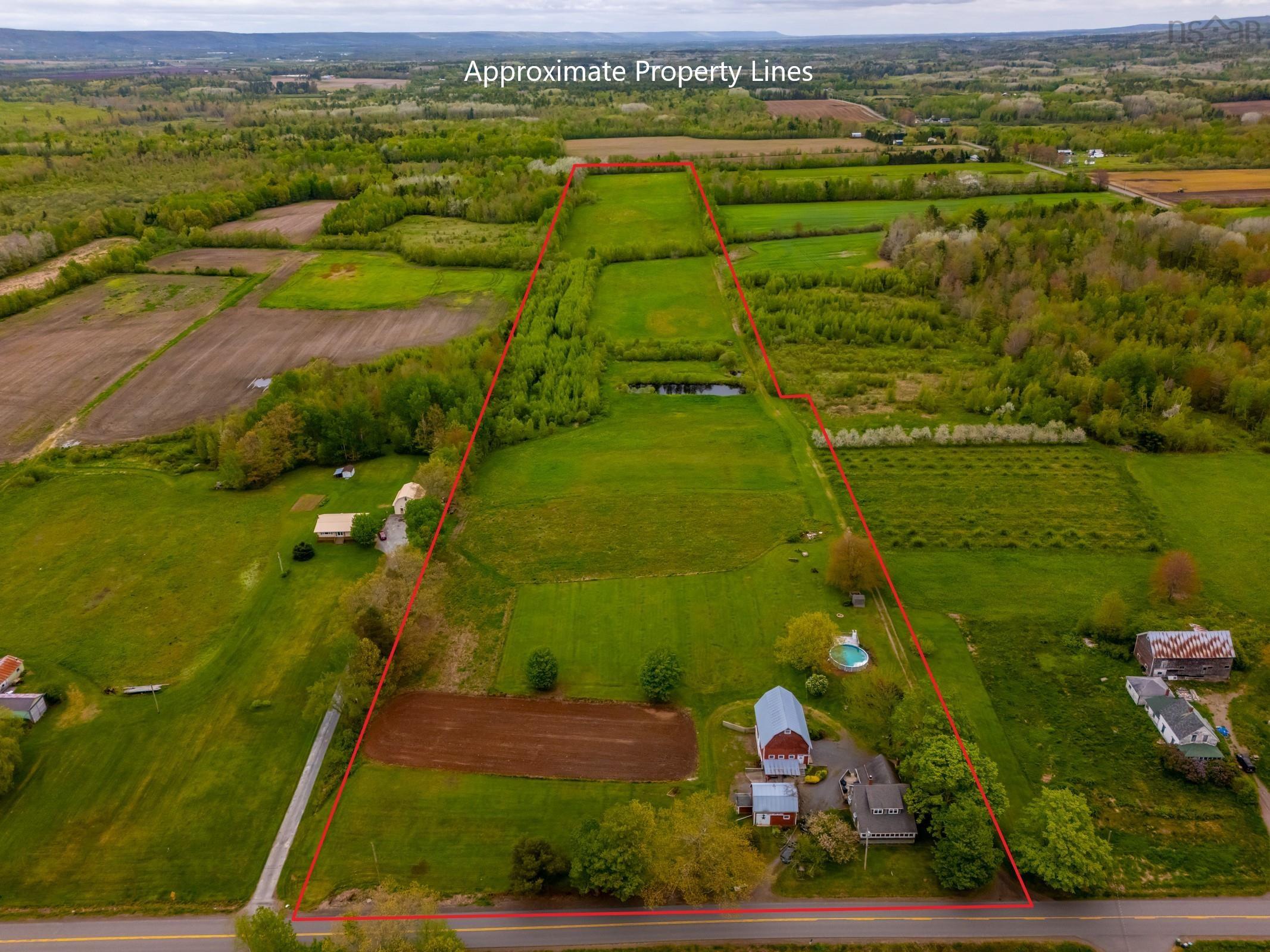 Expansive property featuring vast green fields, wooded areas, and a pond
