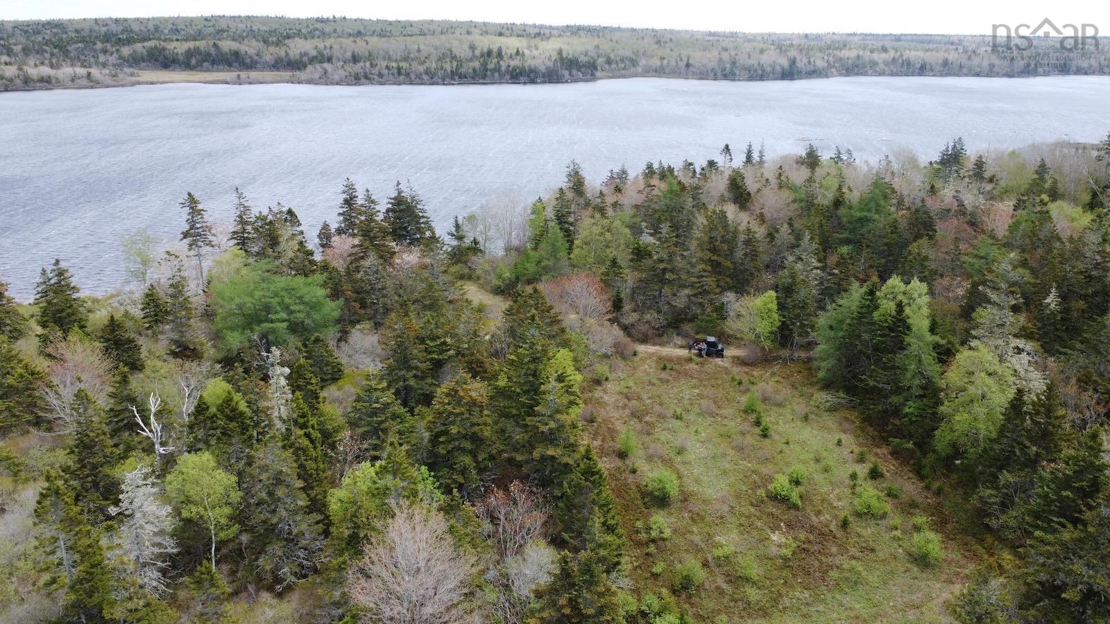 Aerial view of property and surrounding area featuring a heavily wooded area and a nearby body of water