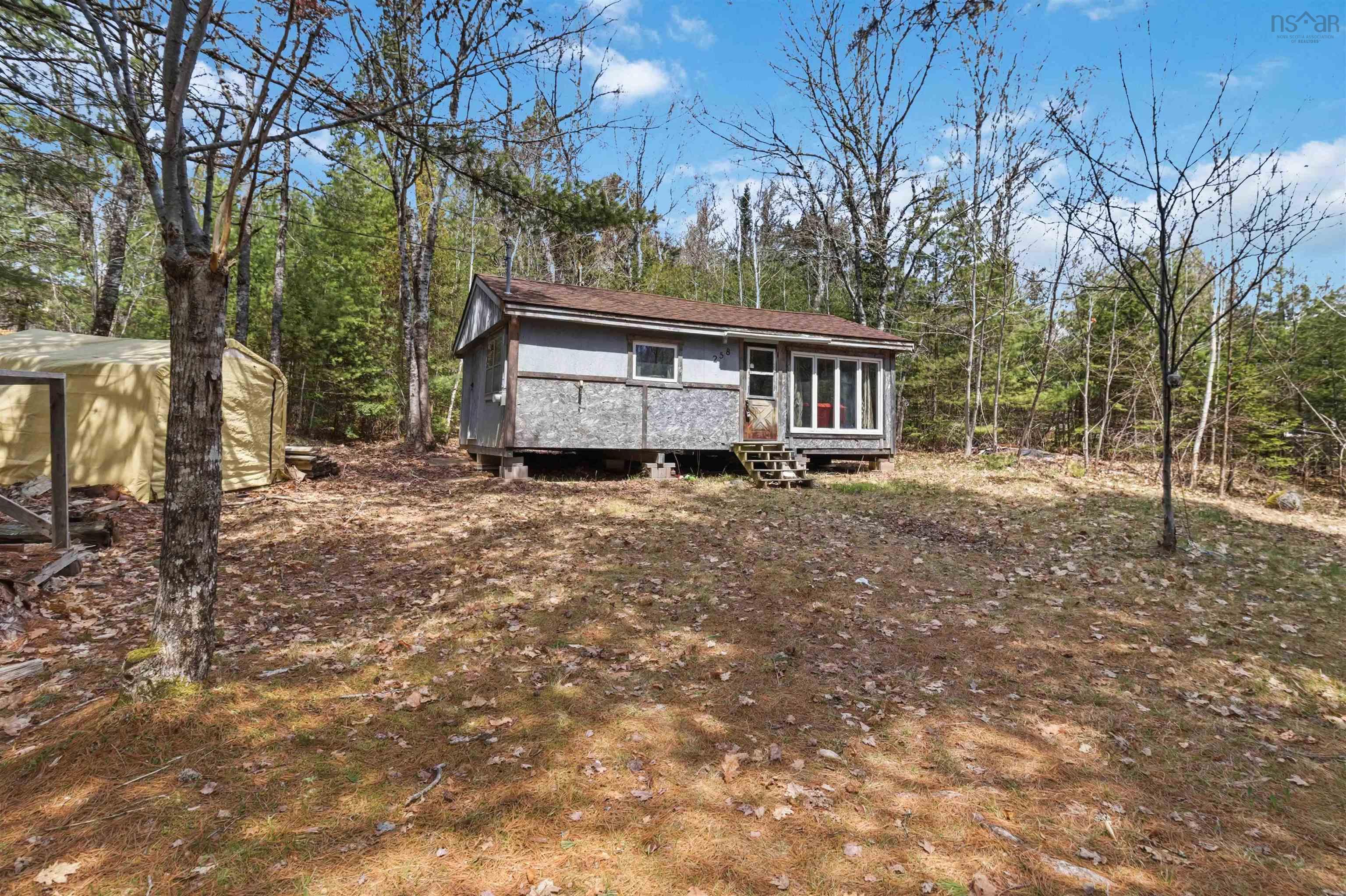 Wooded property featuring a compact cabin with a covered front porch and multi-pane windows