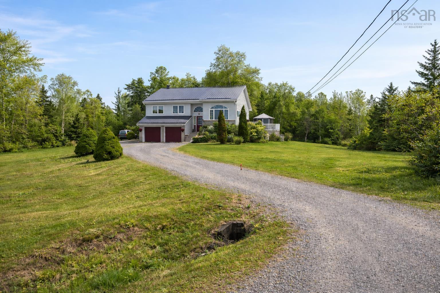 The property features a gravel driveway leading to a two-story residence with a light-colored exterior, a dark roof, and red garage doors